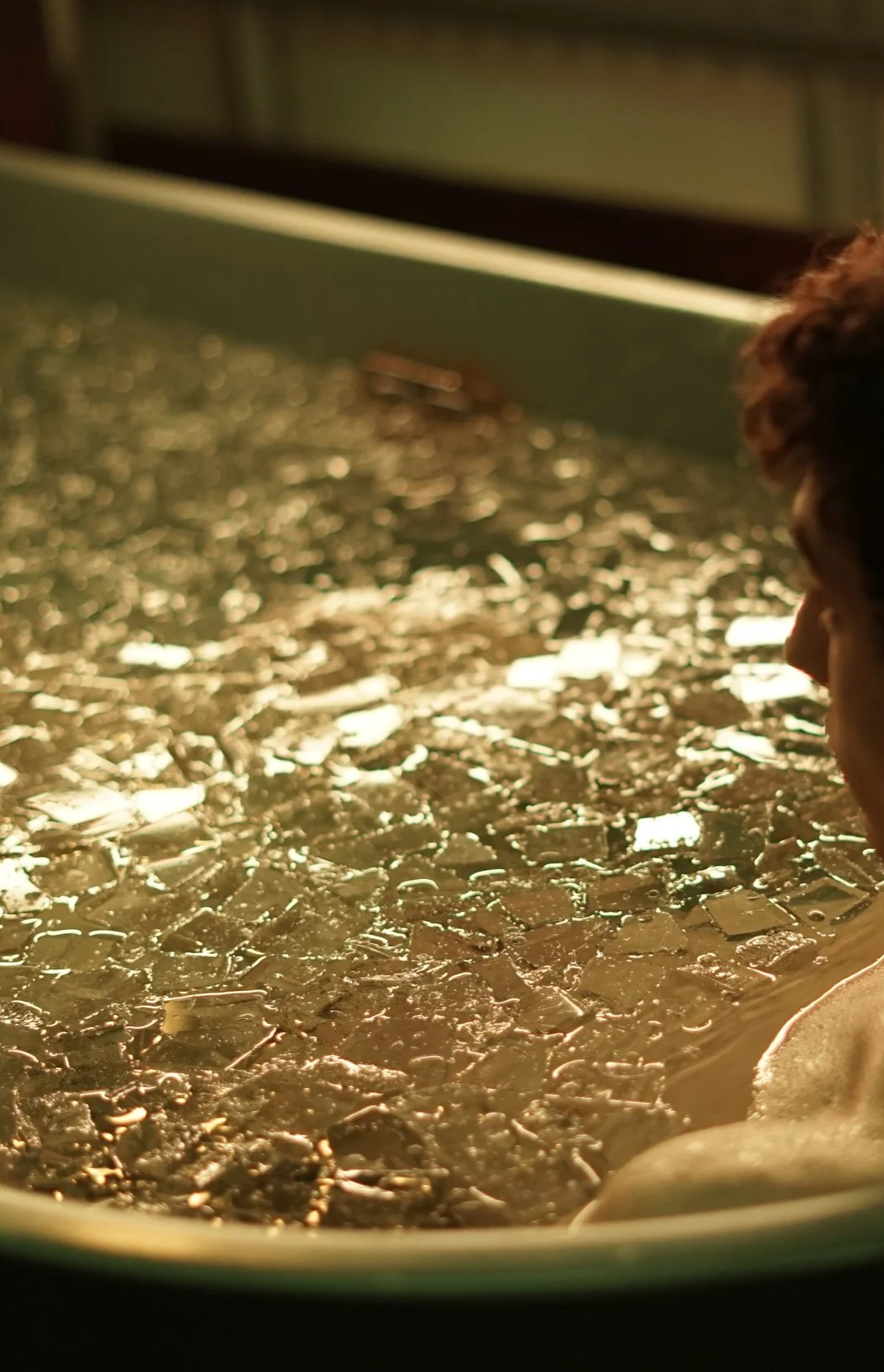 Close-up of a person observing ice cubes melting in a tray under warm light