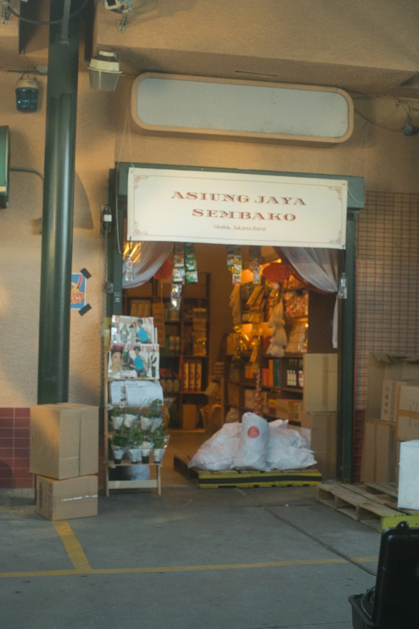 Storefront with a sign reading 'A Sing Jaya Sembako', opening to a space with shelves filled with various goods and items.