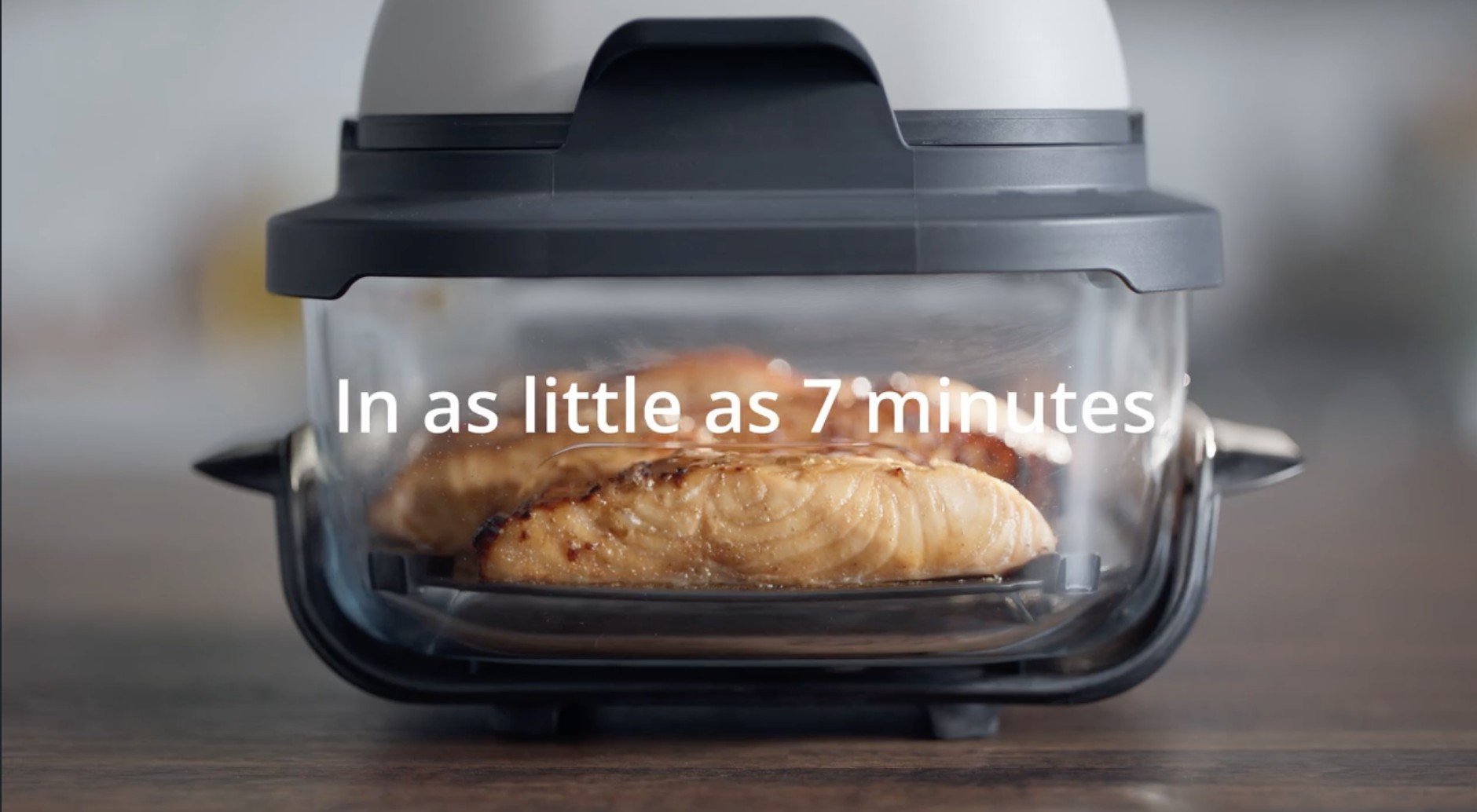 A countertop oven with a glass door cooking salmon fillets, with the caption "In as little as 7 minutes" overlaid.