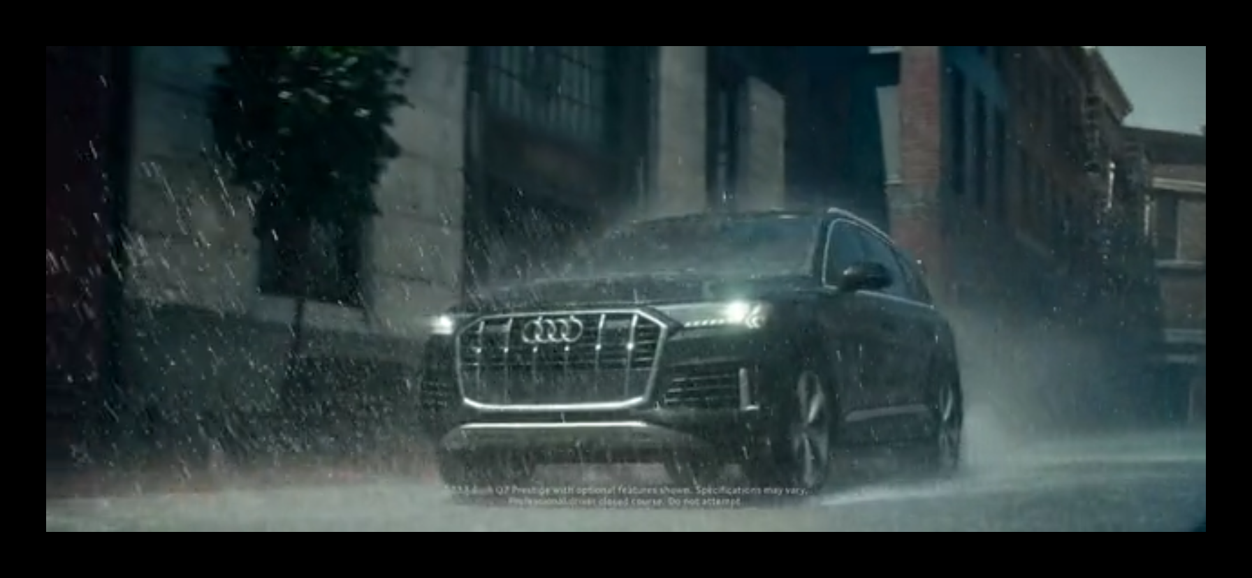 A black Audi SUV driving through heavy rain on a city street at night.
