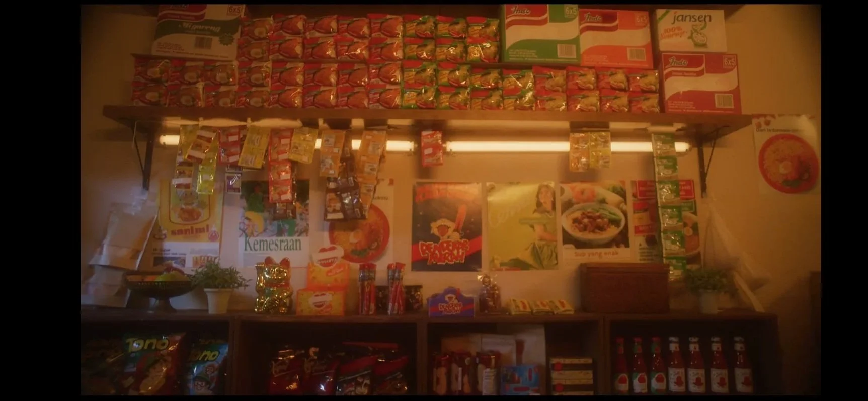 Shelf stocked with various instant noodle cups and packets, with promotional posters on the wall behind.