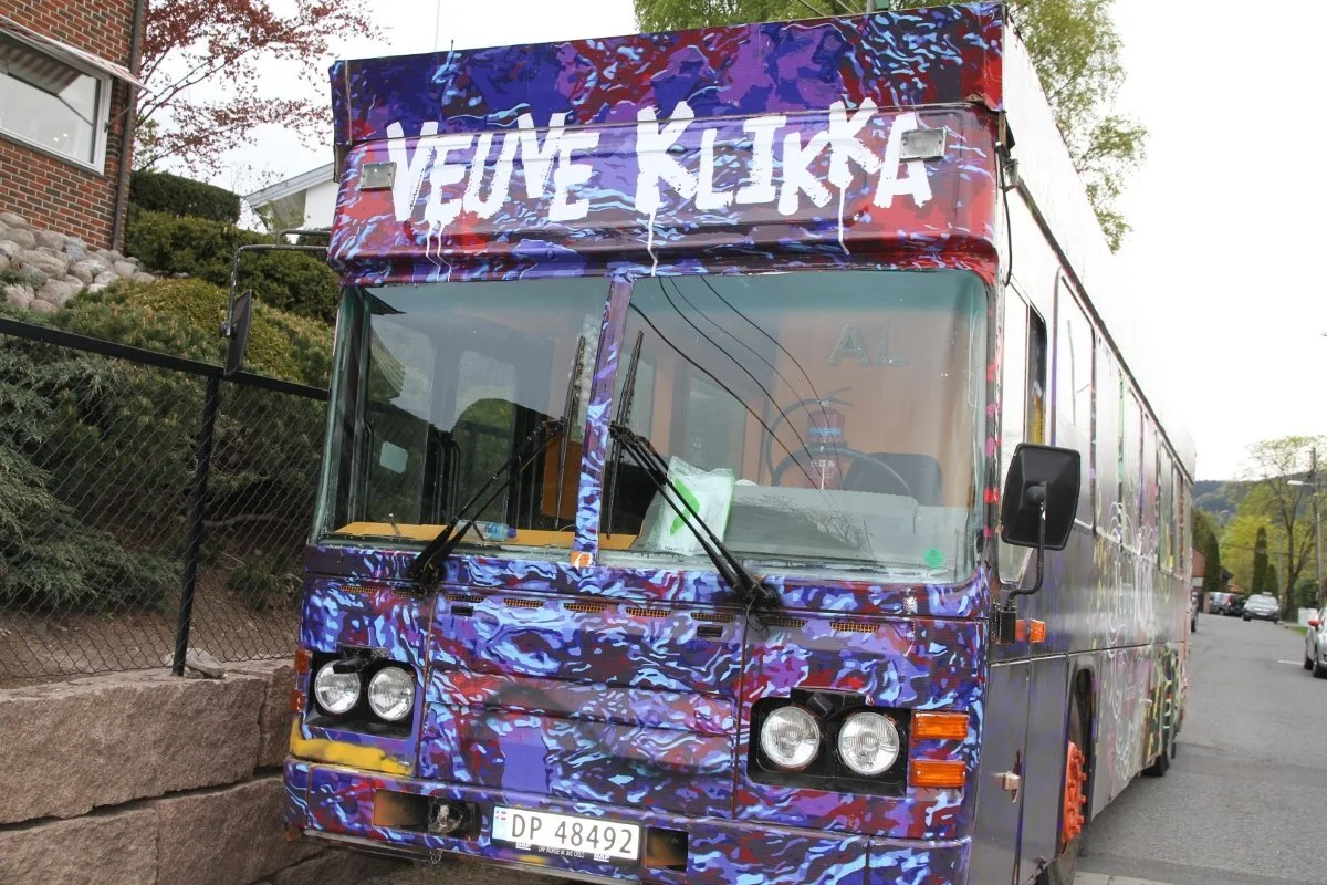 En fargerik buss med graffiti-lignende mønster, med teksten "Velkommen" på forakselen.