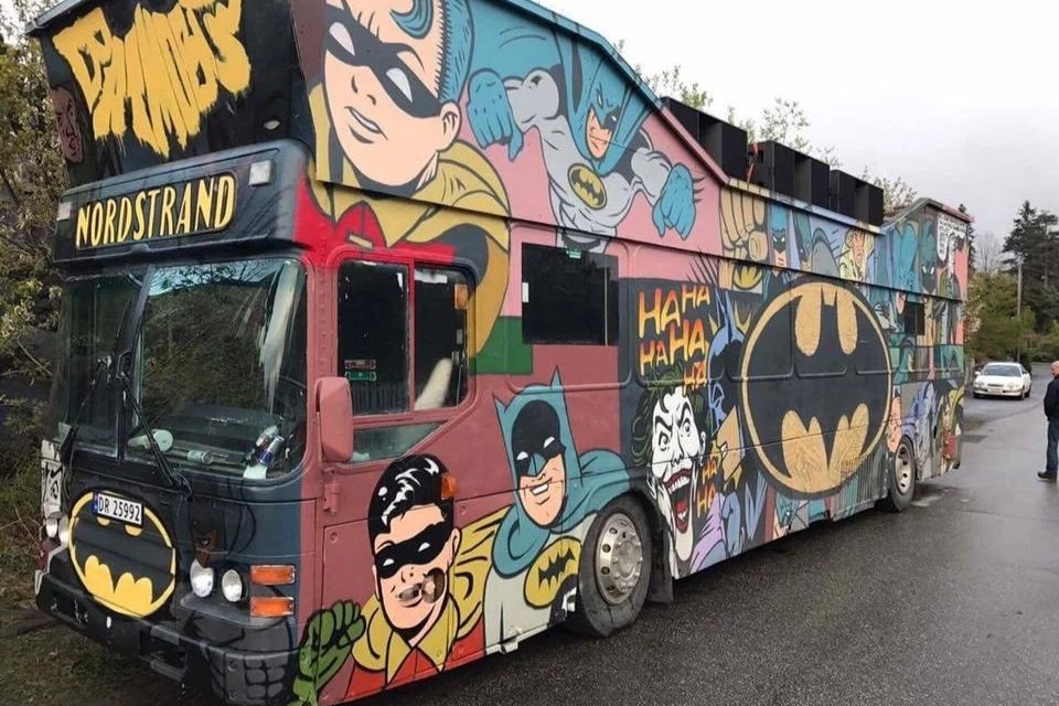 En bus dekorert med tegneseriefigurer av Batman og andre superhelter og skurker, med fargerik graffiti-stil kunst på utsiden.