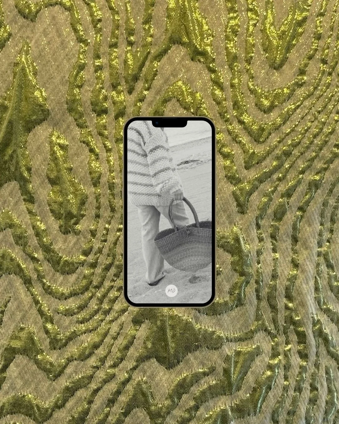 A smartphone displaying a photo of a person in a striped sweater holding a woven basket, with the background of a decorative, shiny gold and green patterned fabric.