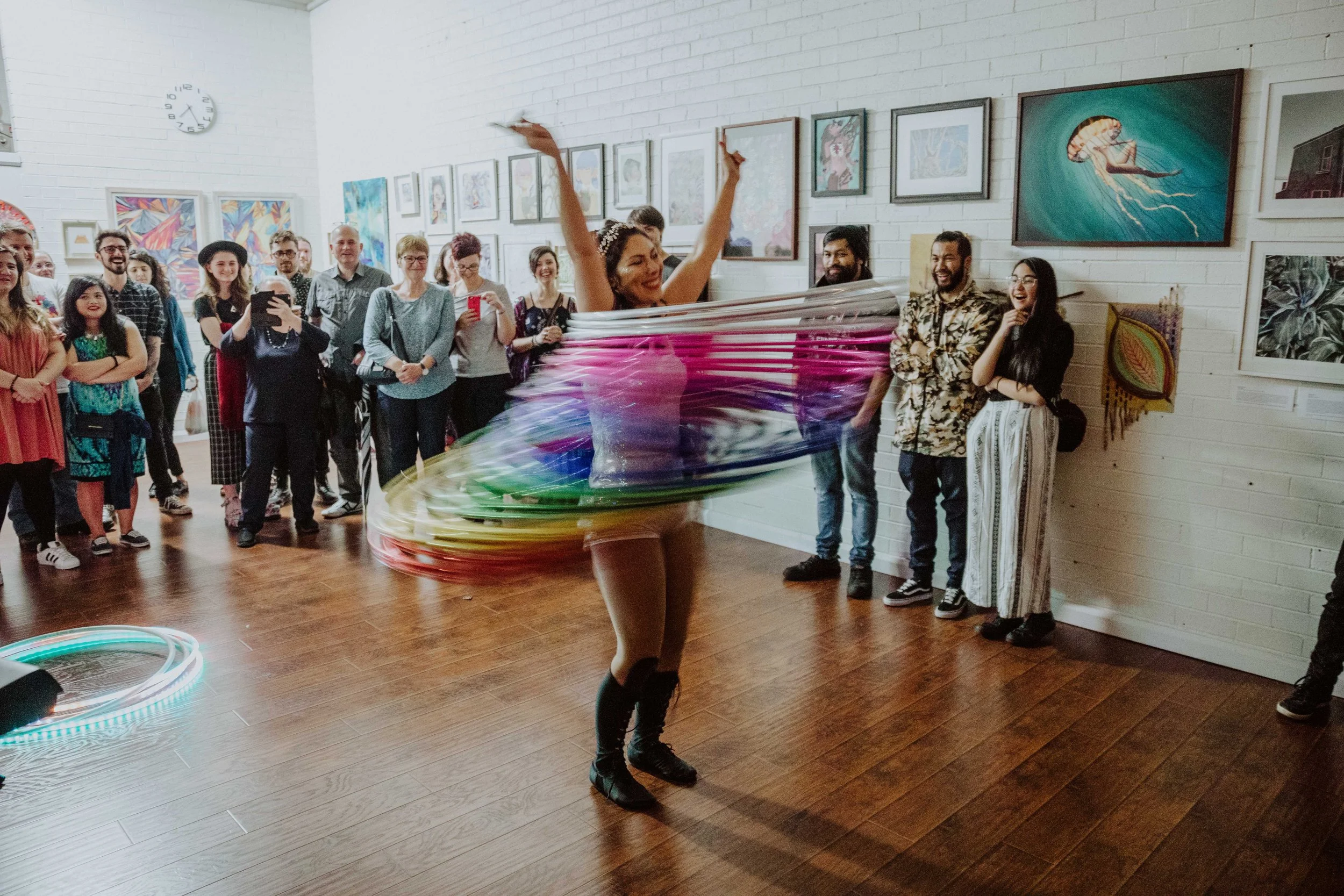 Two women practicing aerial yoga using blue silk hammocks in a room with blue floral wall art and wooden floors.