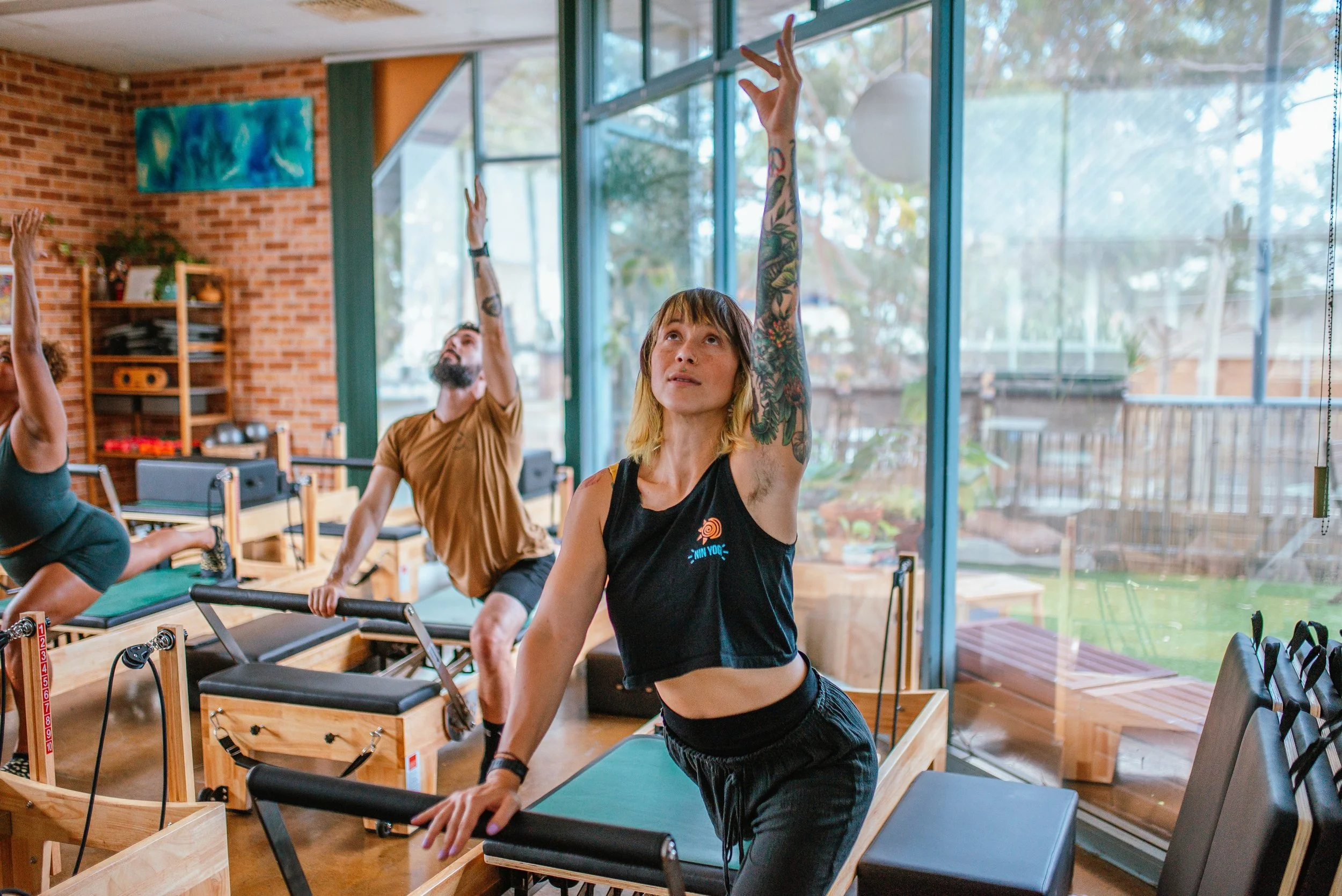 Group of women and girls chatting indoors, with a painting, plants, and shelves in the background.