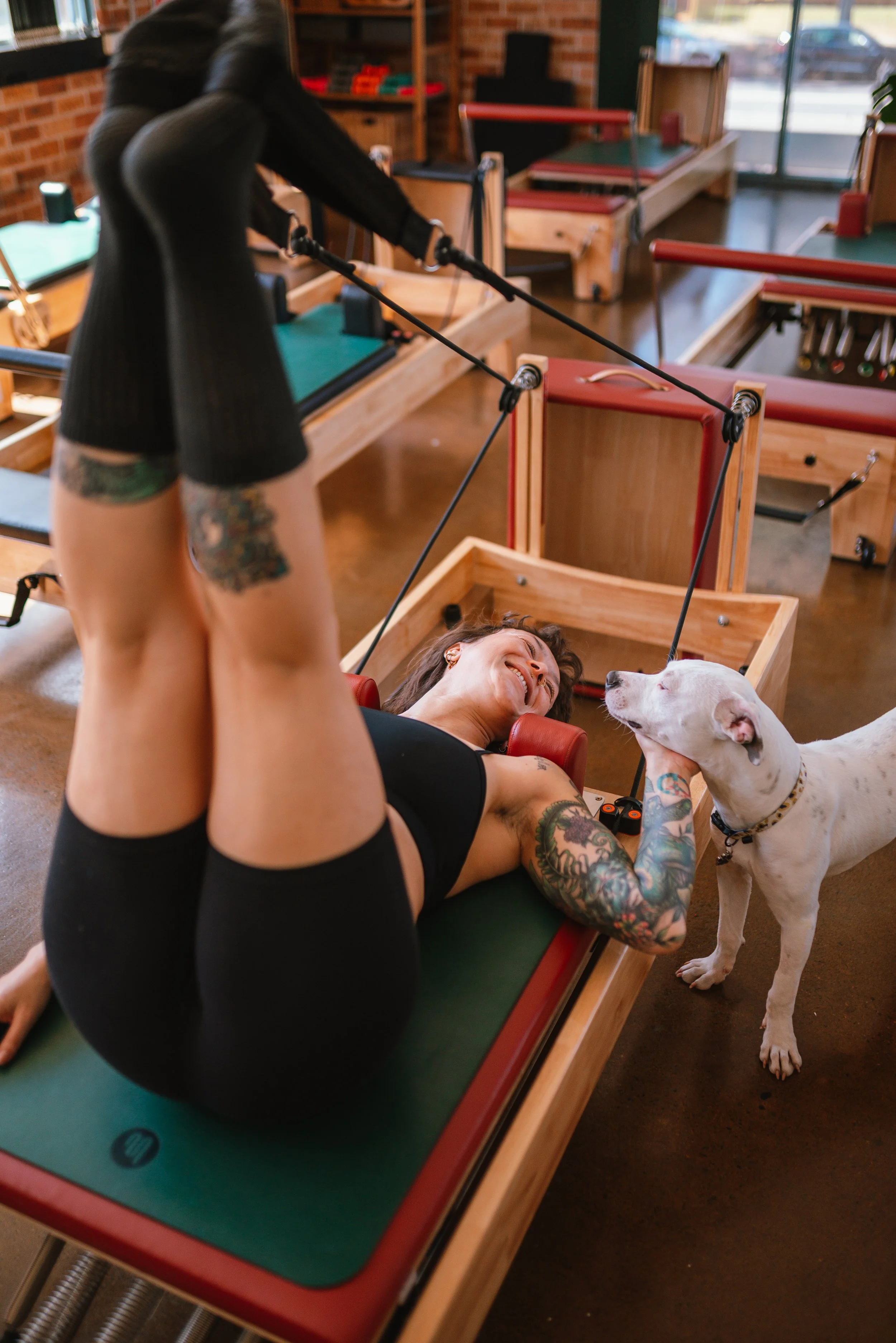 Women participating in a Pilates or reformer exercise class at a fitness studio, smiling and using Pilates reformer machines.