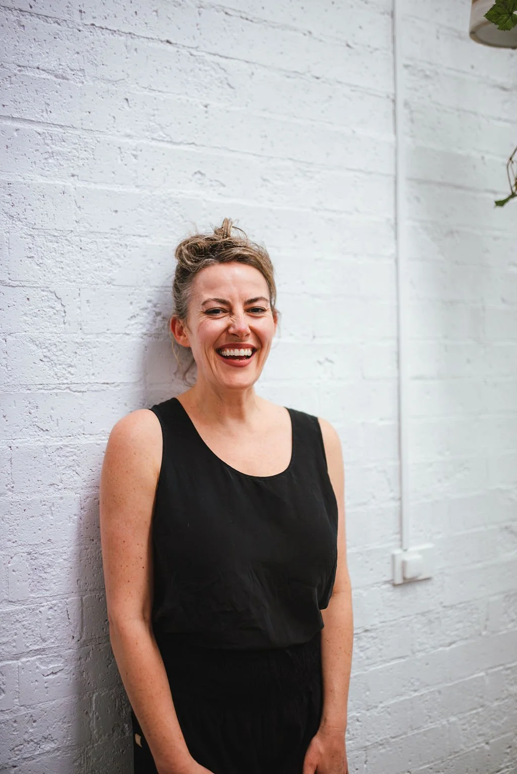 A woman wearing a black shirt smiling and standing in front of a white brick wall