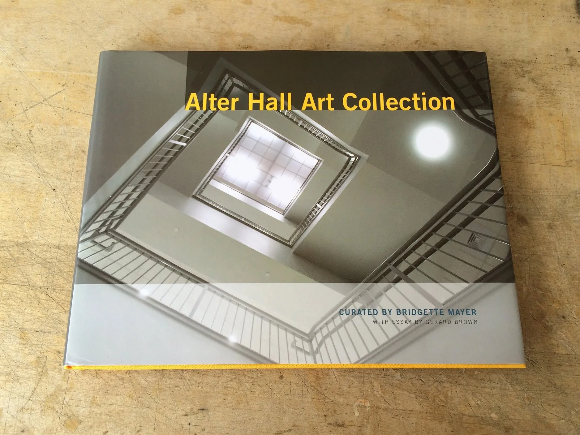Book titled 'Alter Hall Art Collection' with a cover photo of a stairwell looking up at a ceiling light fixture, curates by Bridgette Mayer, with an essay by Gerard Brown.