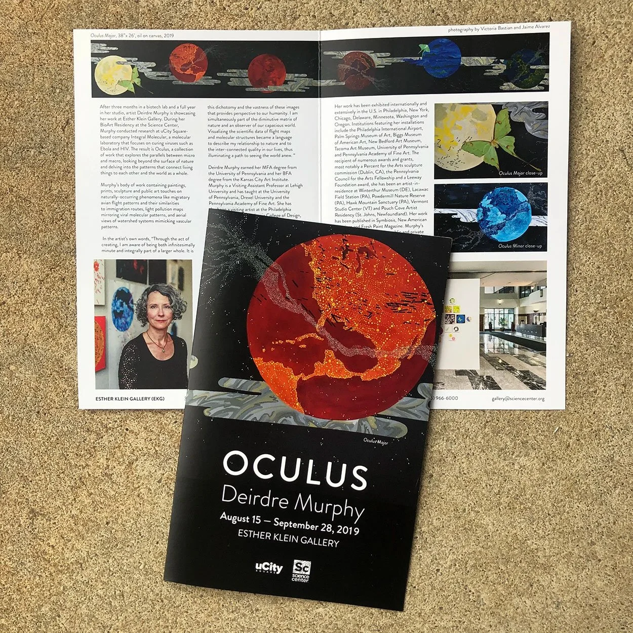 Flyer and brochure for the "Oculus" art exhibit by Deirdre Murphy at Esther Klein Gallery, September 2019. The design features colorful planetary images, with the foreground showcasing a black brochure with a vivid red and orange planet illustration,