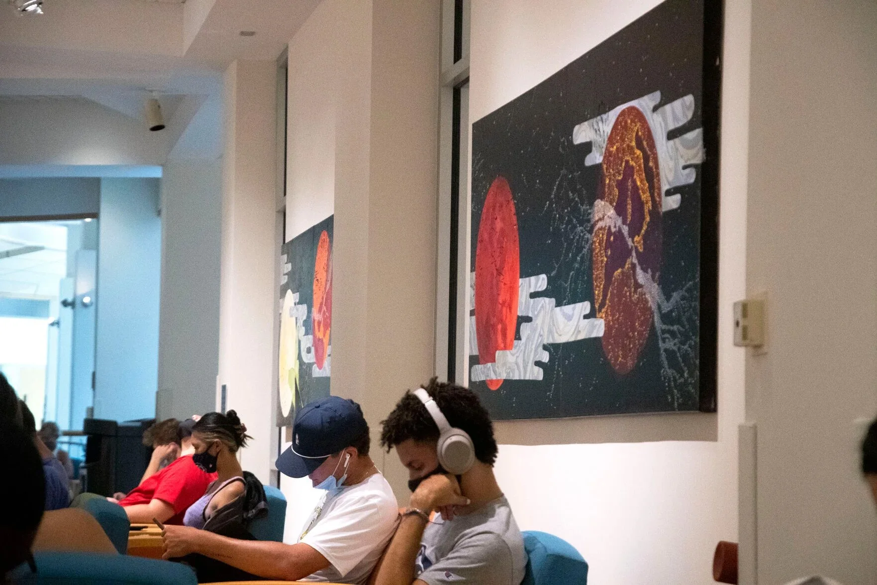 People seated in chairs, some wearing masks, in a room with modern artwork on the wall.