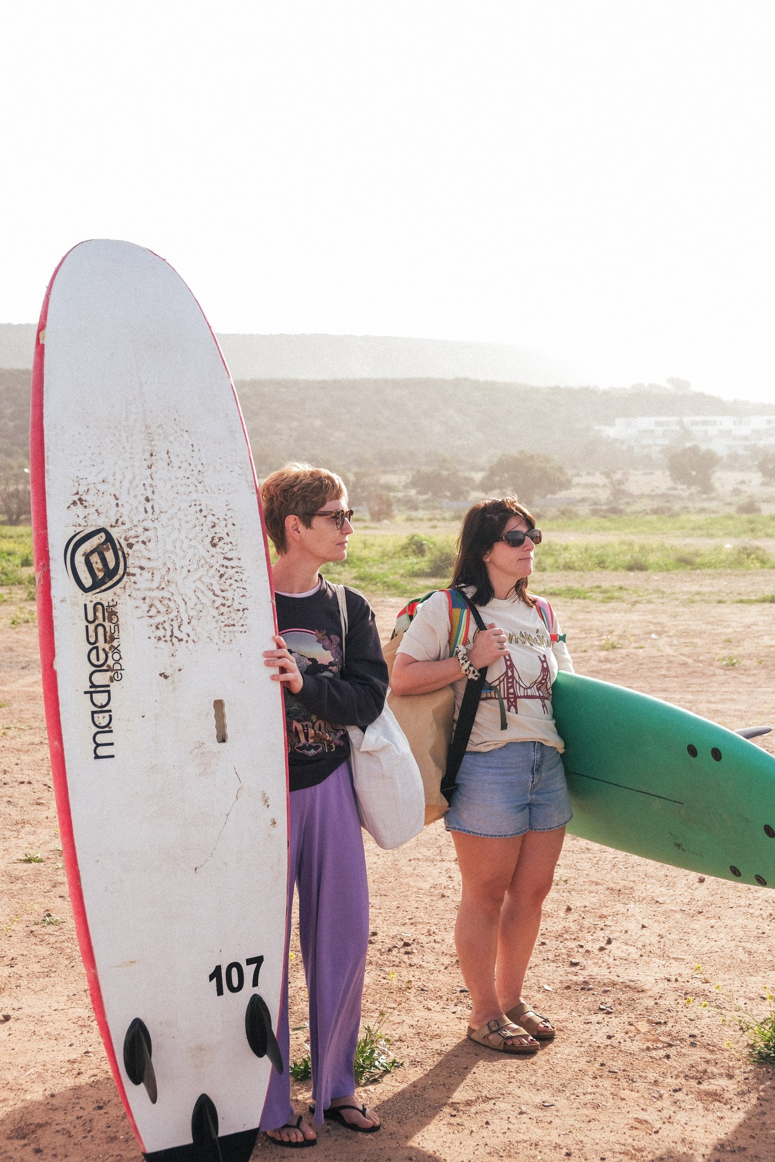Deux participantes portant leurs planches de surf profitent d’un moment calme avant une session, dans la lumière douce de la plage au Maroc.