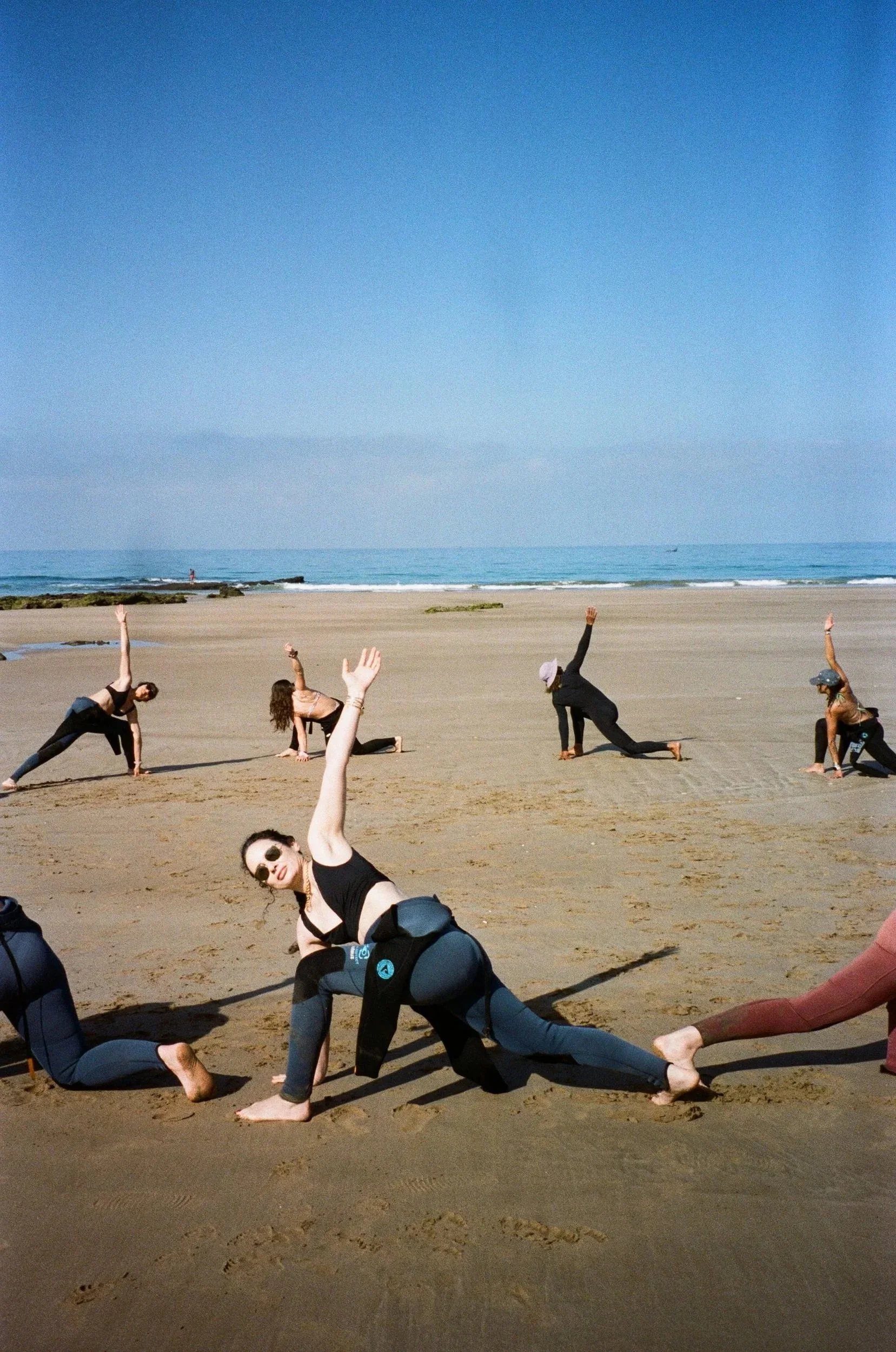 Groupe de personnes pratiquant le yoga ou le stretching sur la plage, avec la mer et le ciel bleu en arrière-plan.