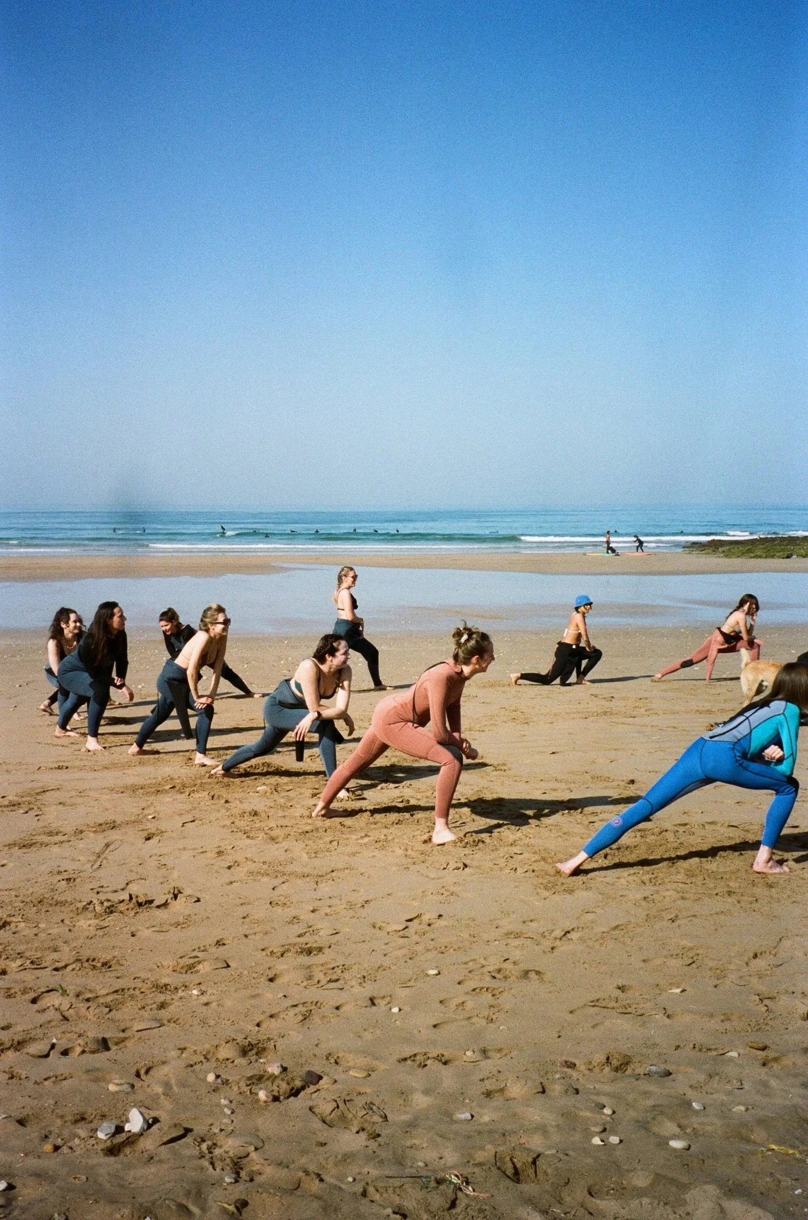 Groupe de personnes faisant du yoga sur la plage sous un ciel bleu, avec l'océan en arrière-plan.