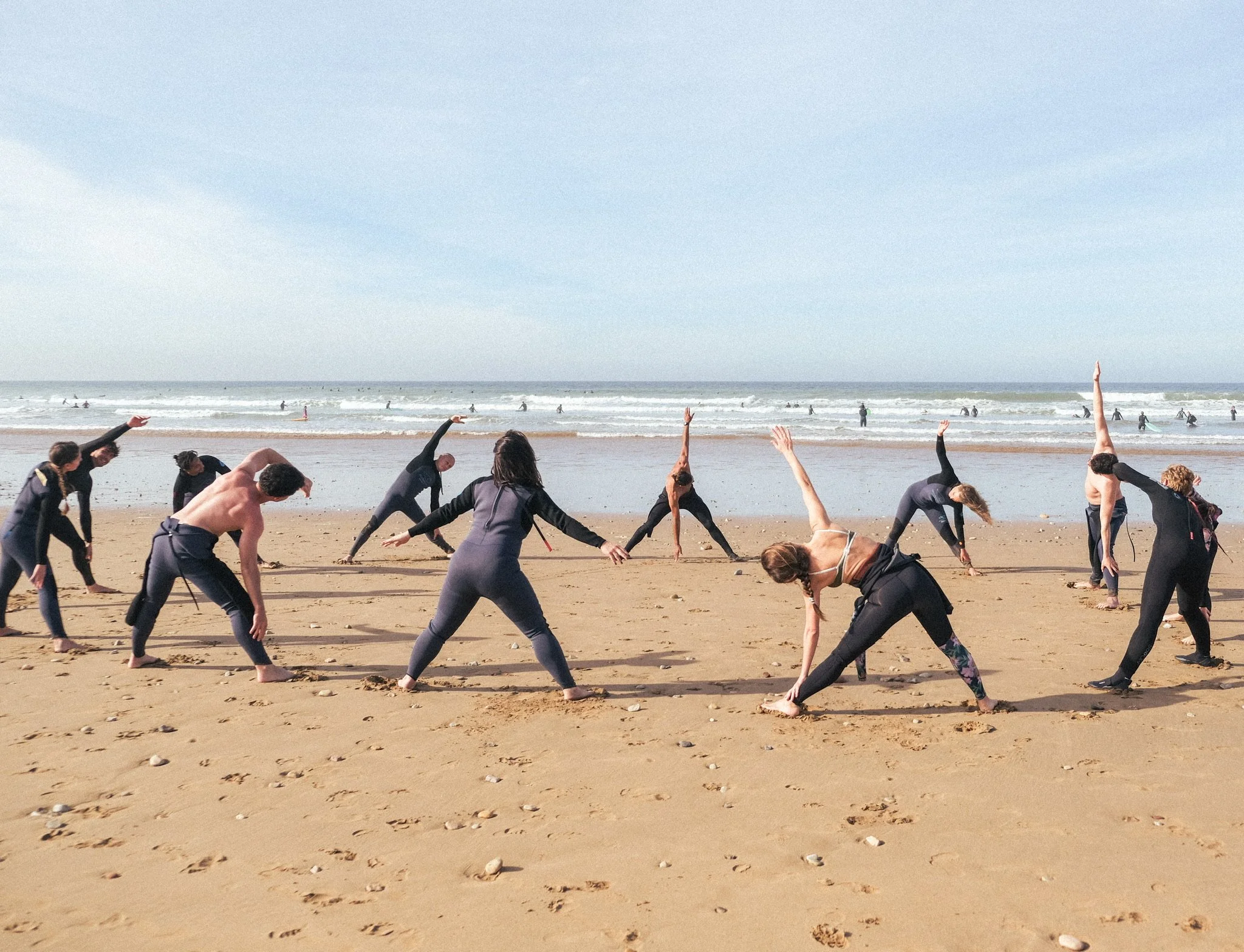 Séance d’étirements collective sur la plage face à l’océan, pour préparer le corps avant une session de surf dans une ambiance sportive et conviviale.