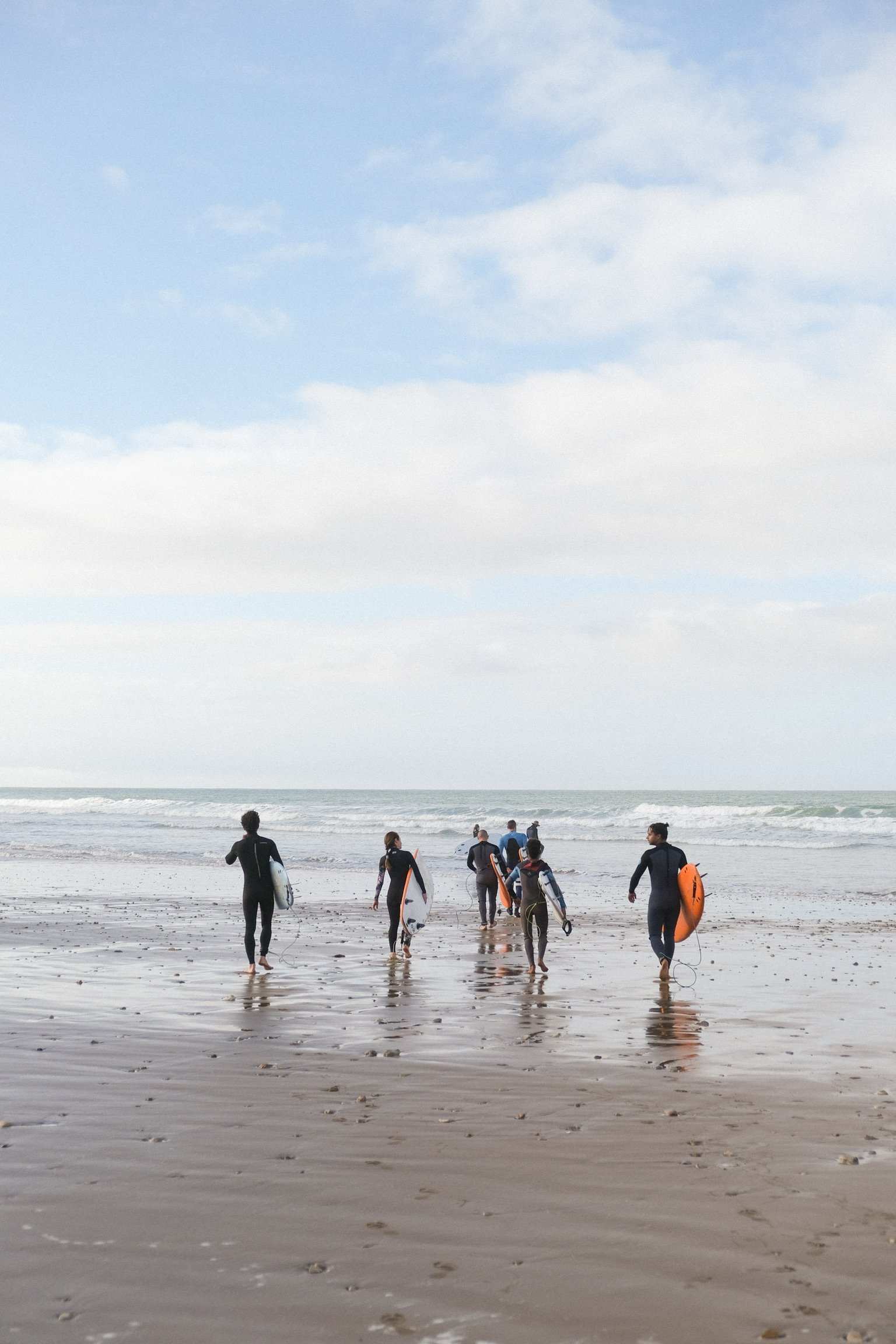Groupe de participants marchant vers l’océan avec leurs planches de surf, prêts à rejoindre les vagues sur la plage de Tamraght.