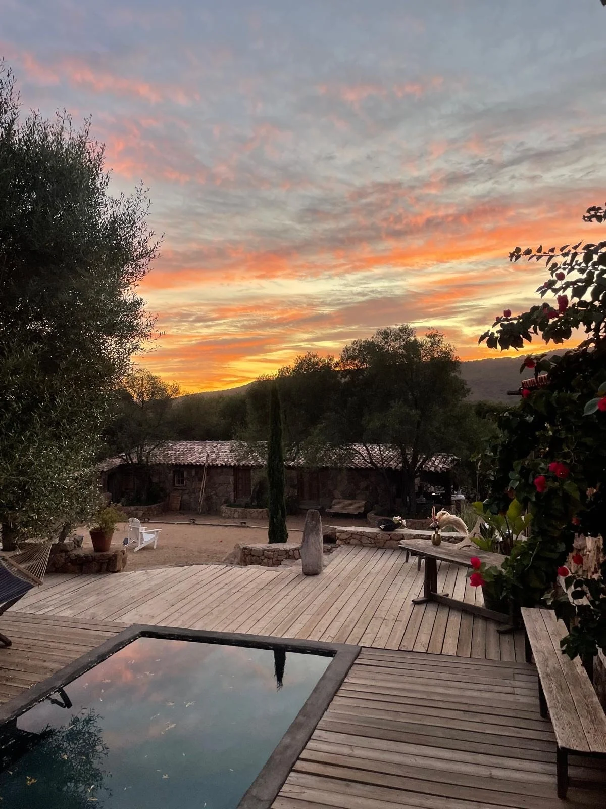 Coucher de soleil sur une cour intérieure avec piscine, arbres et bâtiment en pierre, ambiance calme et naturelle.