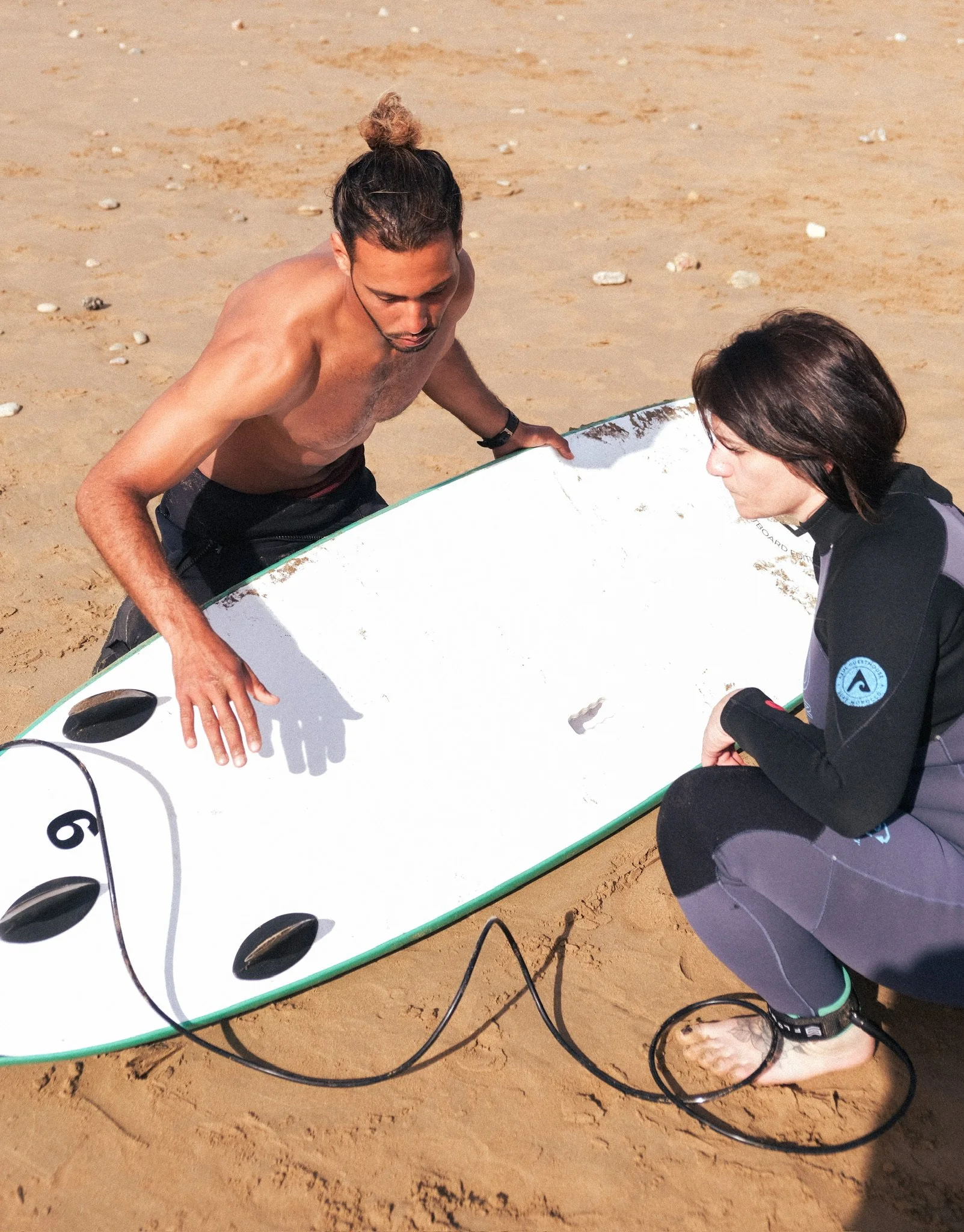 Un moniteur de surf explique les bases techniques sur la planche à une participante, lors d’un cours sur la plage au Maroc.