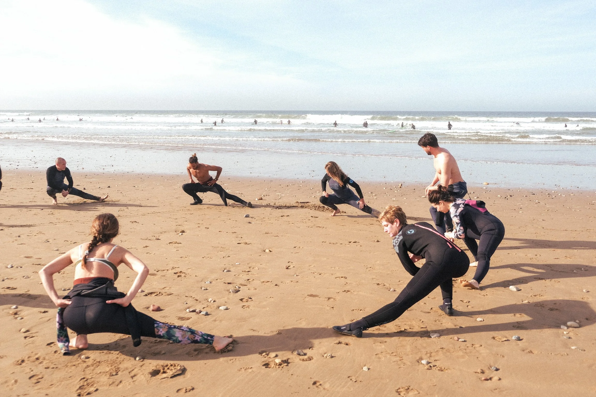 Groupe de participants en plein échauffement sur la plage avant une session de surf, face aux vagues et à l’océan au Maroc.