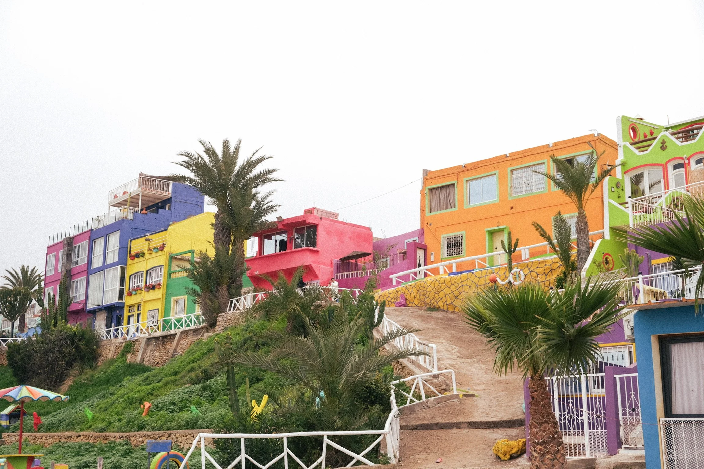 Maisons colorées et palmiers dans un village côtier marocain, une ambiance chaleureuse et dépaysante au cœur de la région de Taghazout.