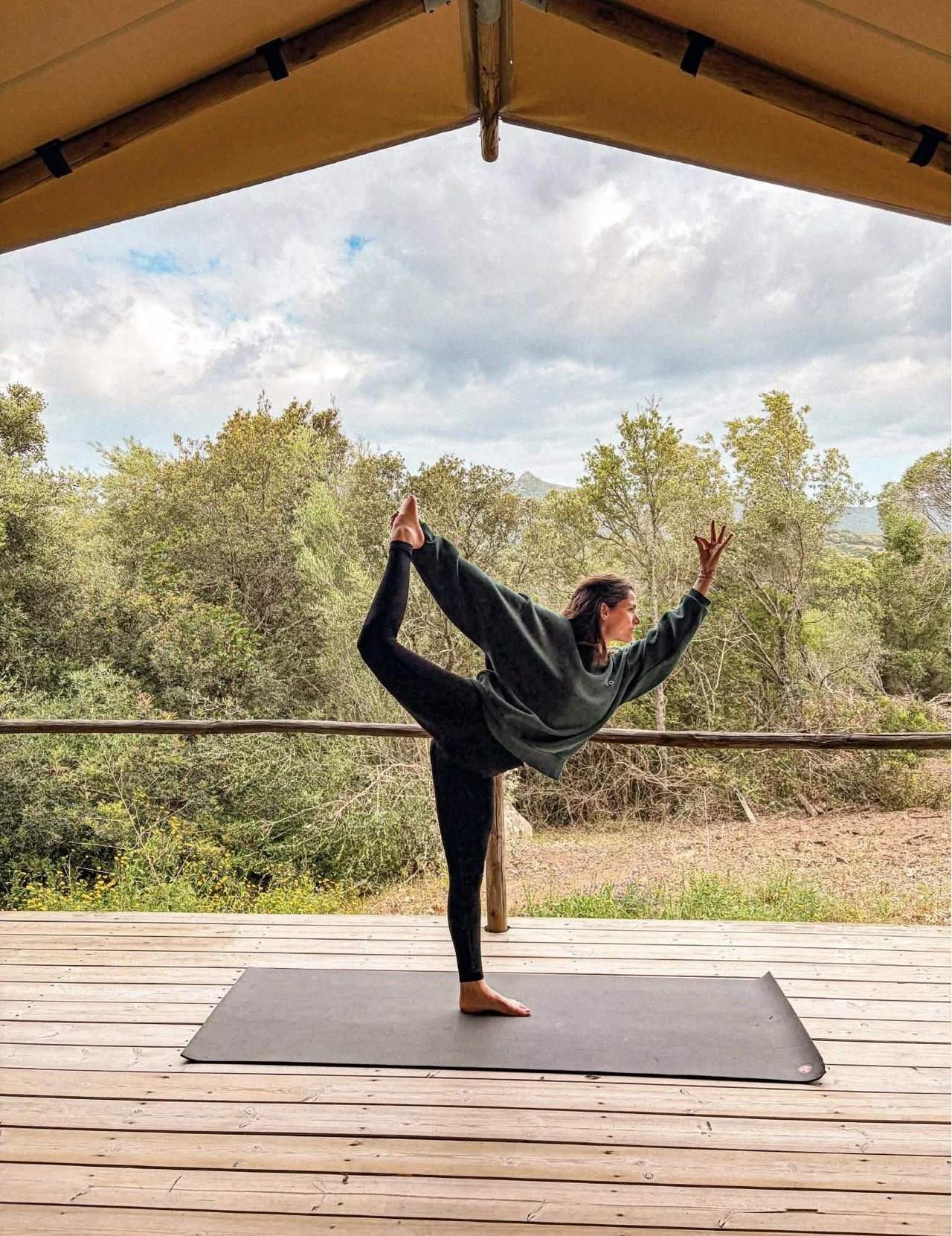 Une femme pratique la yoga sur un tapis en extérieur, sous un dolmen, avec une forêt en arrière-plan, en position de détente.