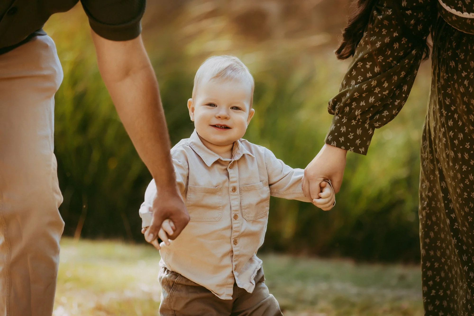 A smiling young boy holding hands with two adults outdoors during autumn. Unposed Hobart family photography.