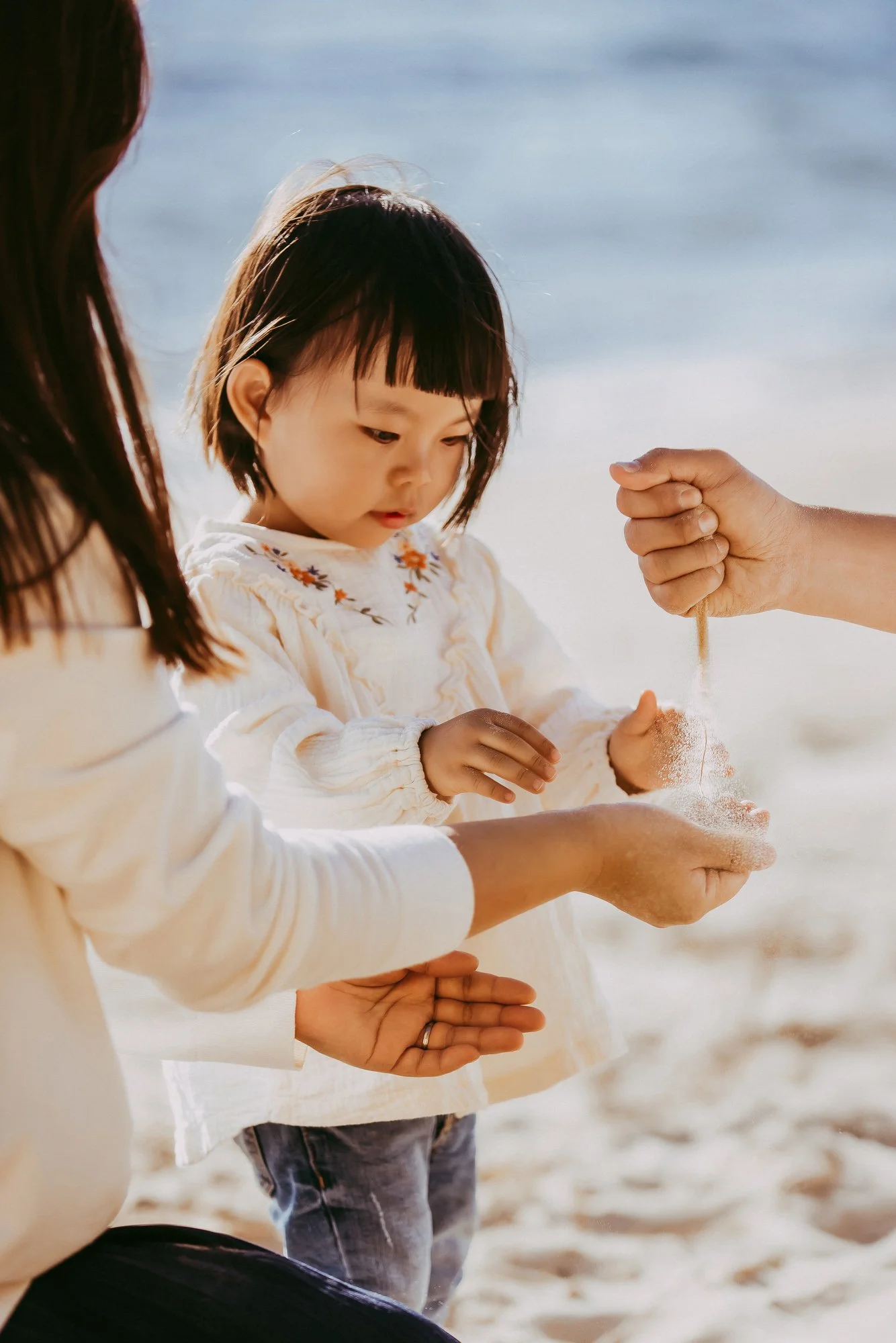 A young girl on the beach being helped to sift sand through her hands by adults. Affordable family photosession in Greater Hobart.