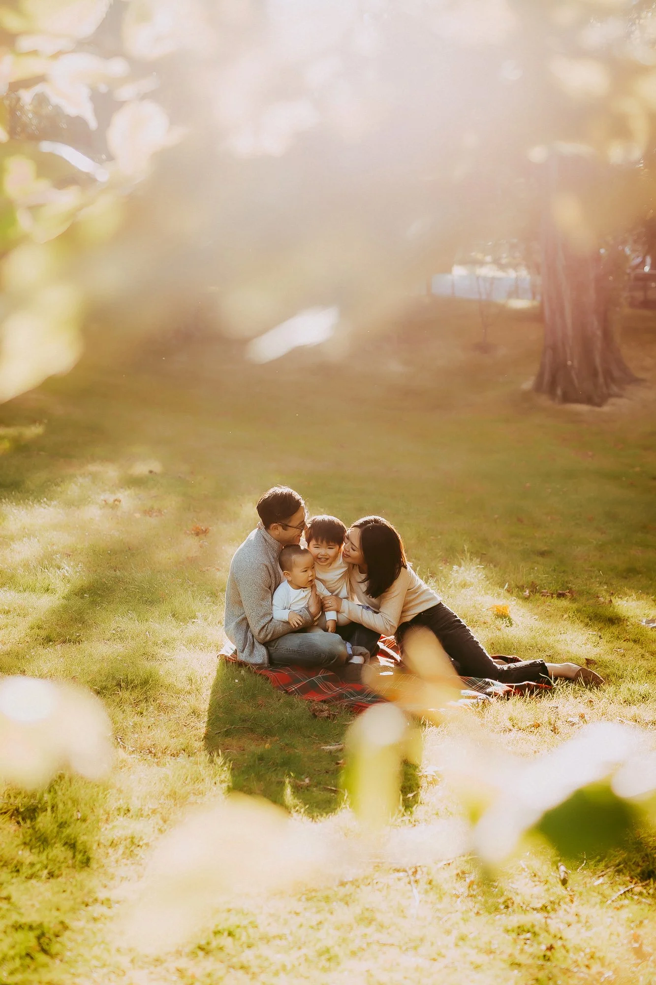 Family of four sitting on a blanket in a park during sunset, smiling and laughing together. Cascade Brewery family photography session.