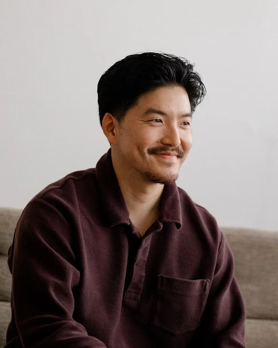 Victor sitting on a beige sofa, smiling softly, against a plain white wall.