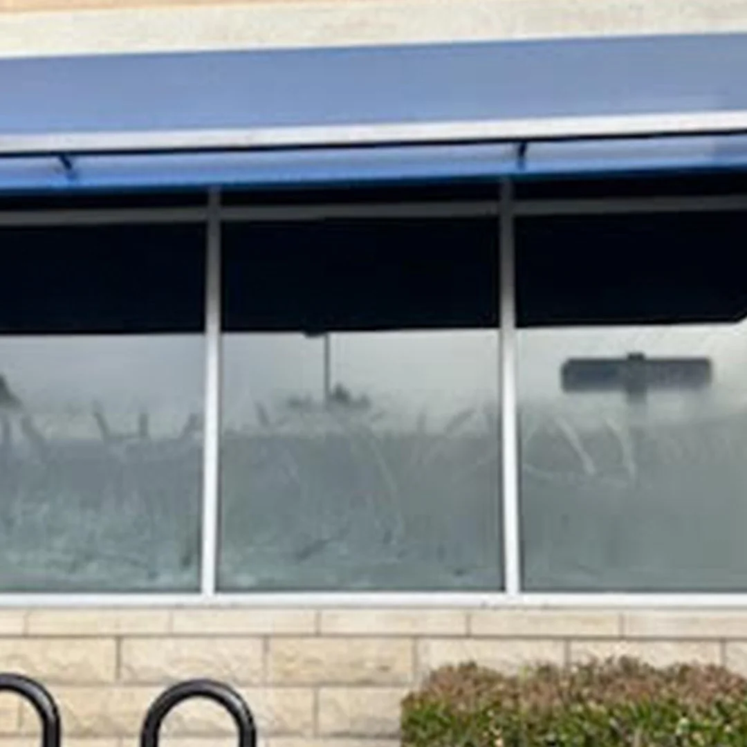 "Technician applying clear anti-graffiti film to a commercial storefront window to protect against vandalism and surface damage"