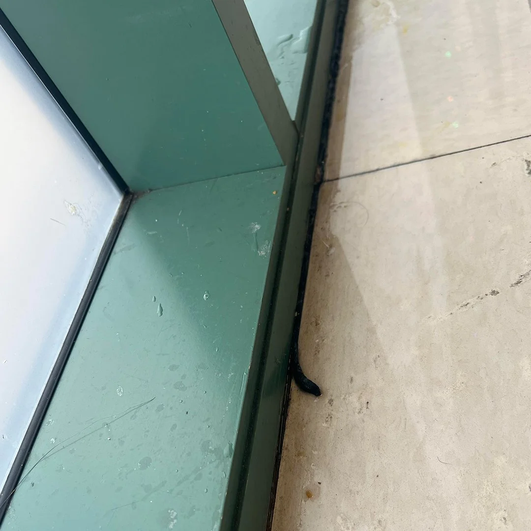 "PH Glass technician sealing window edges with waterproofing materials to prevent water intrusion in a commercial building"