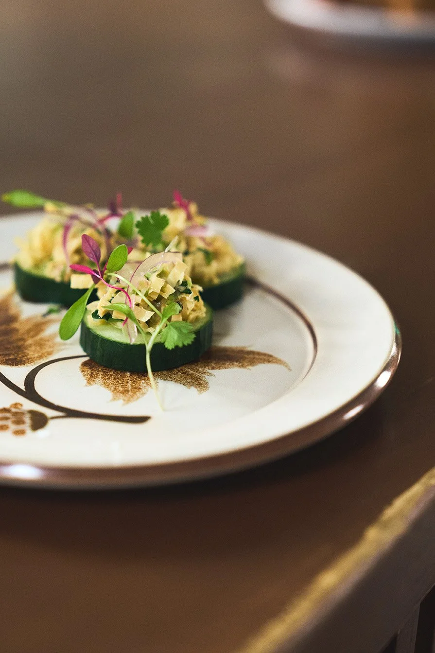 Close-up of two cucumber slices topped with chopped vegetables and microgreens on a decorative plate.