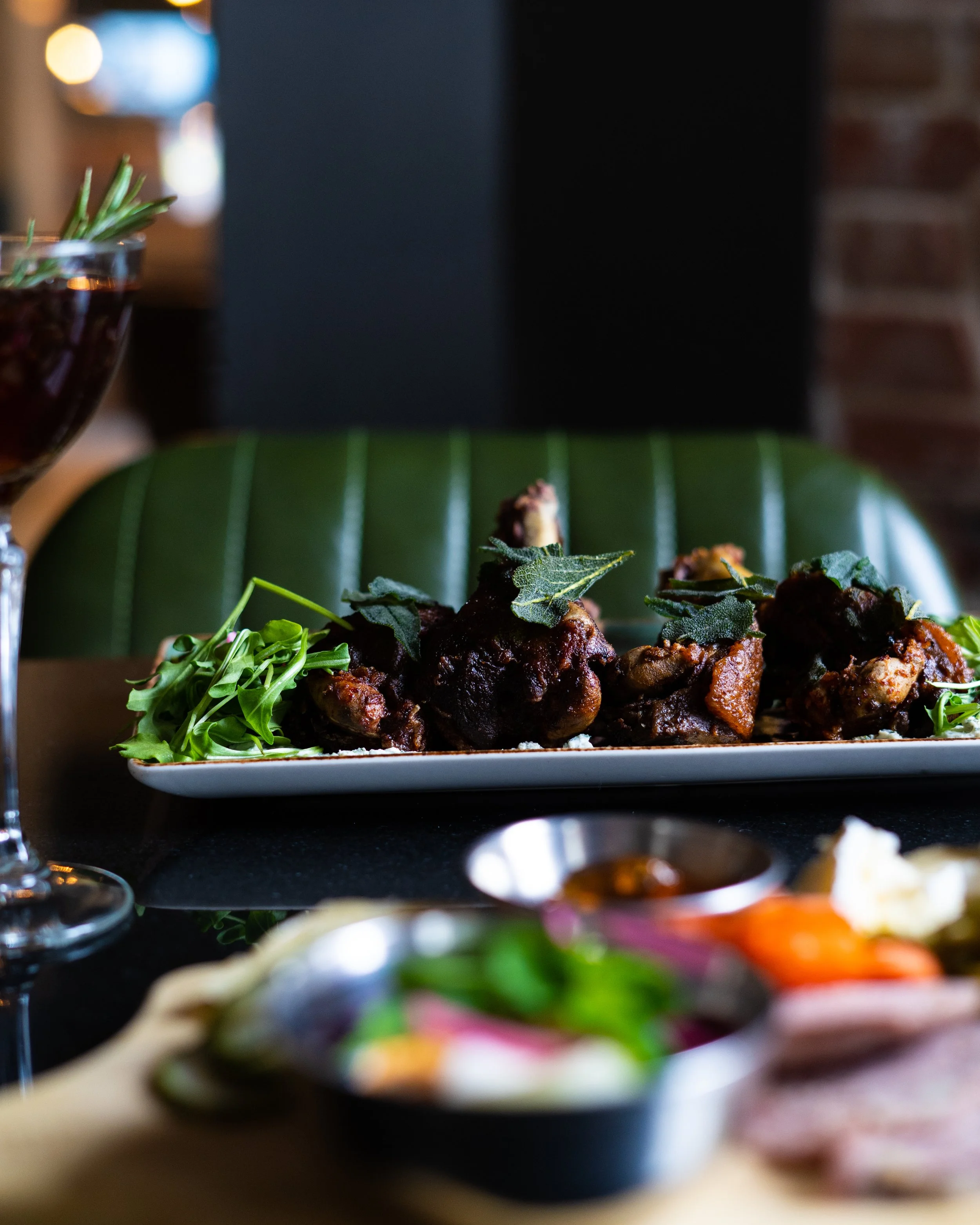 Close-up of a dish from The Clarendon tavern of meat garnished with herbs, a sprig of greenery on the side, in a restaurant setting with a blurred background. Photographed by Gumption Studio, Ottawa food photographer.