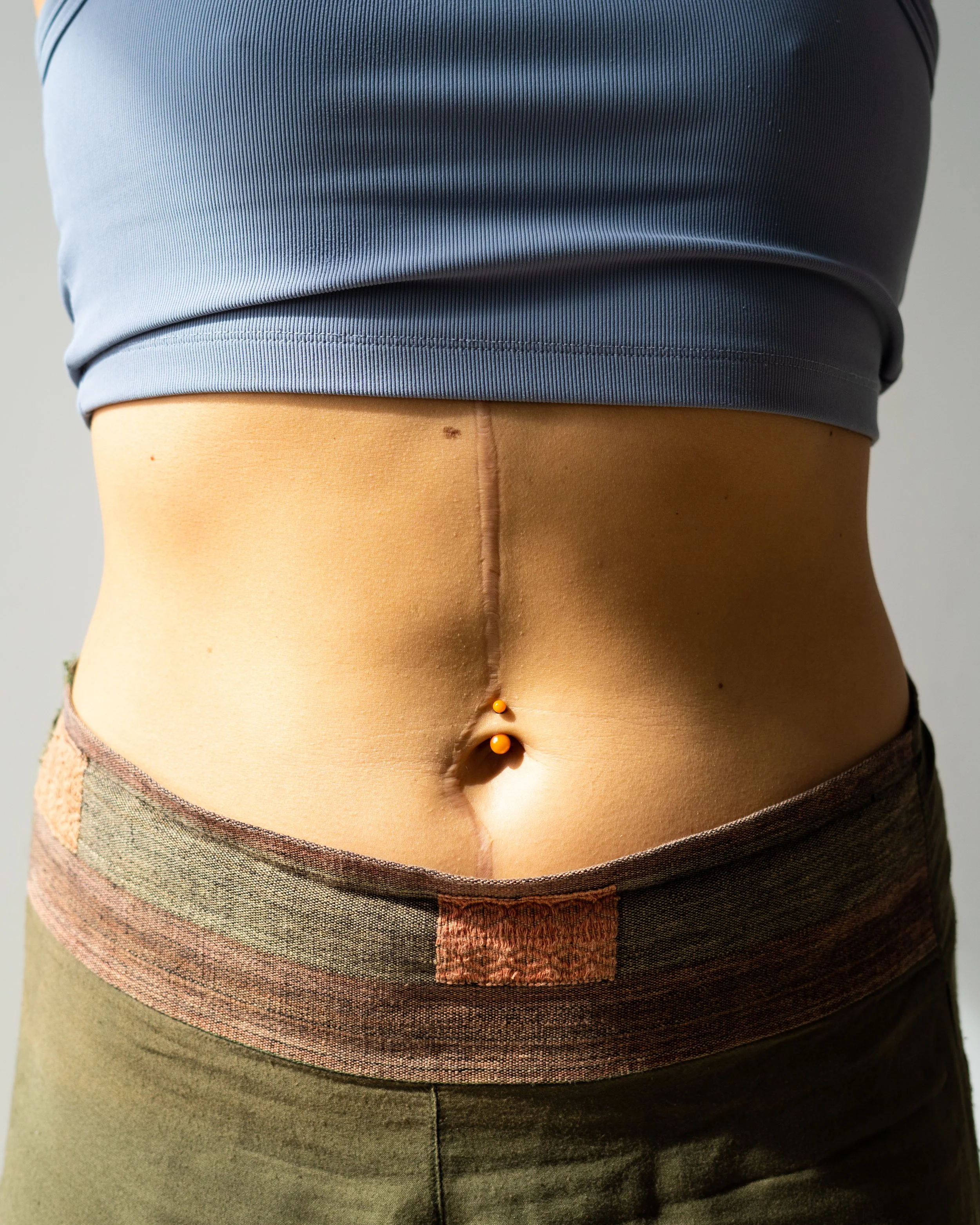 Close-up of the waist and hips of a mannequin wearing a blue t-shirt and multi-colored striped shorts with a jean button fly.