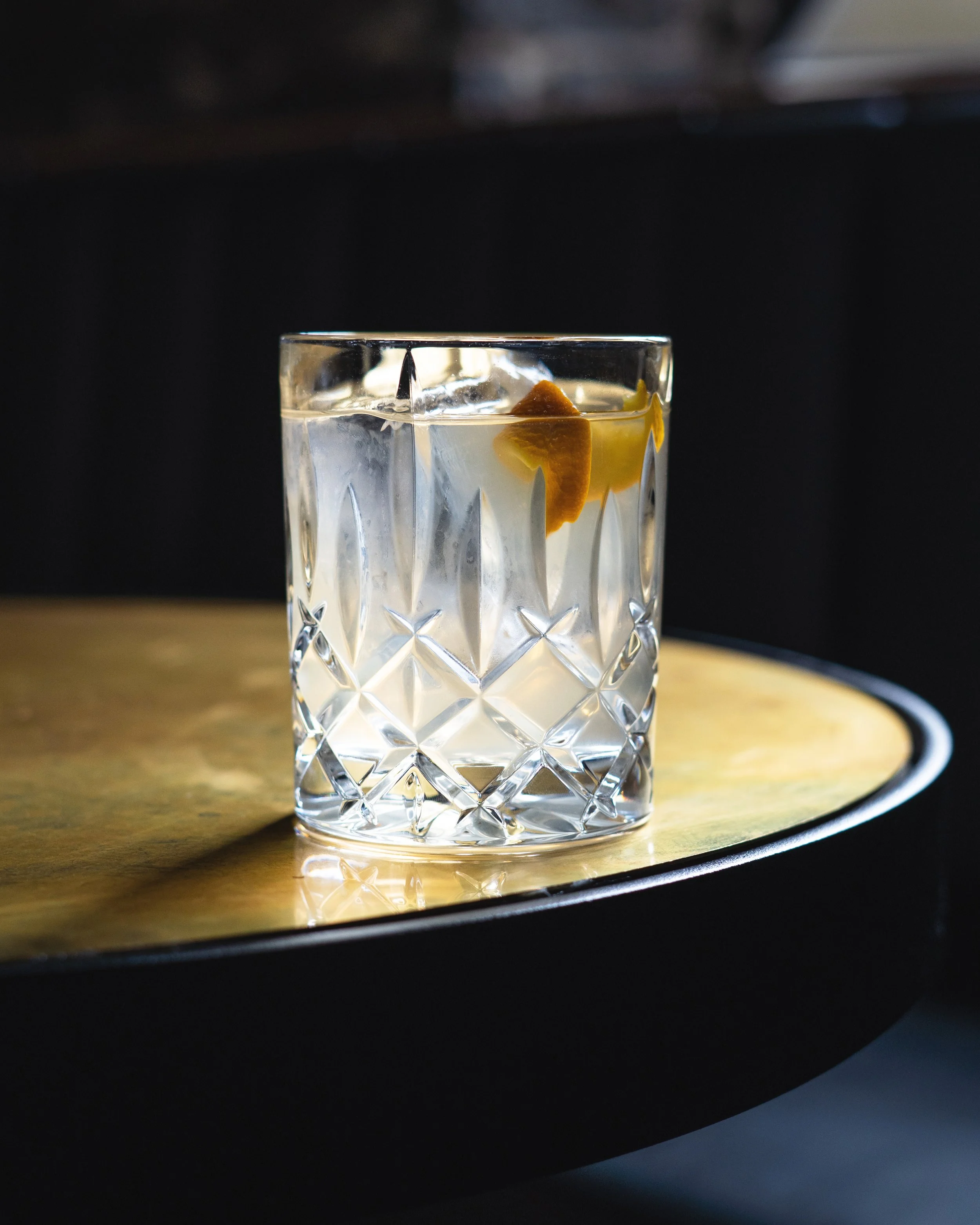 A clear Negroni at The Hyde, placed on a round brass table, with a dark background. Photographed by Gumption Studio, Ottawa photographer. 