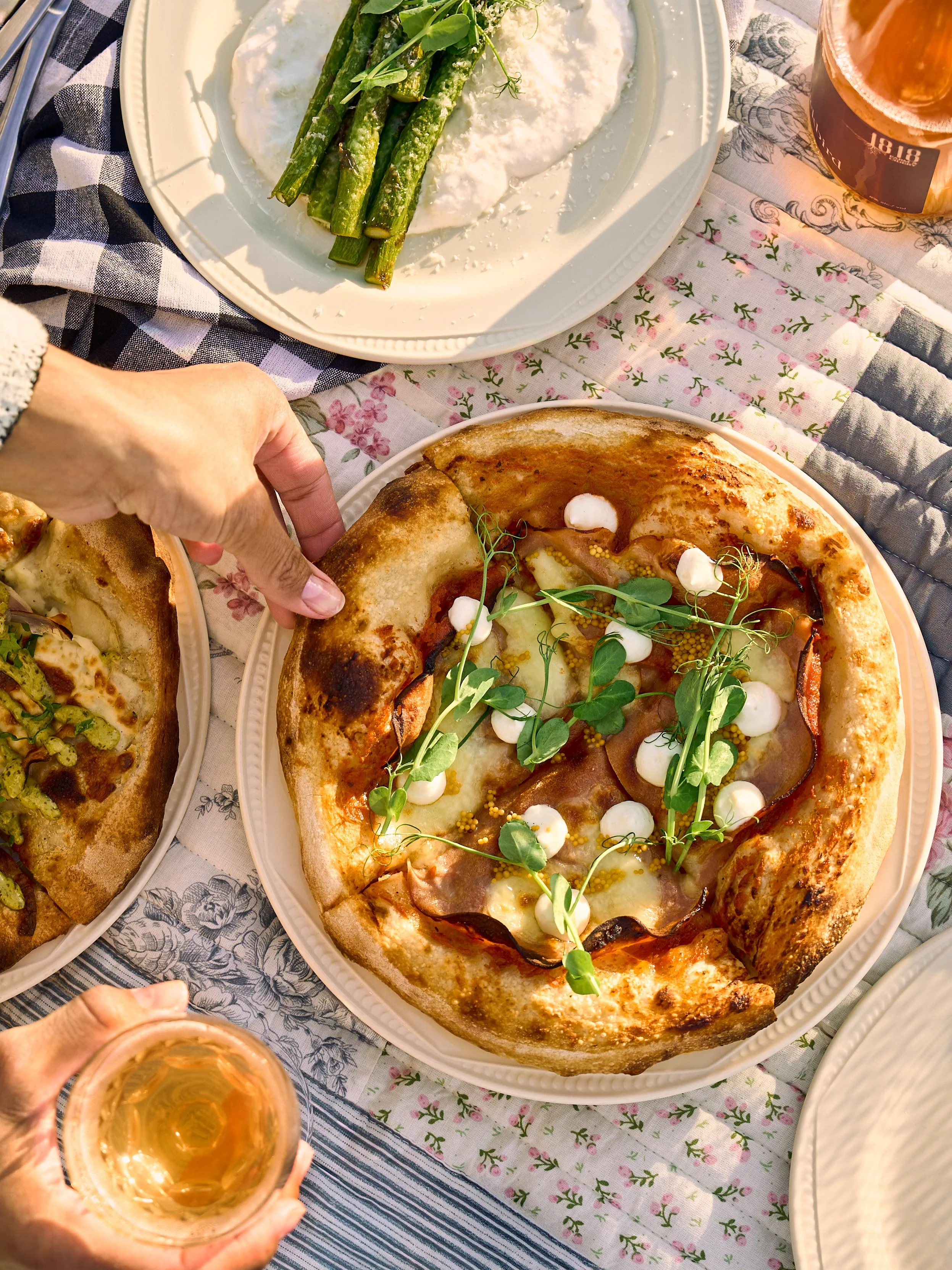 A picnic blanket at 1818 Farm and Cidery with a pizza, a plate with asparagus, a glass of cider, and a person holding a glass. Photo by Ottawa Photographer Sarah Farmer of Gumption Studio.