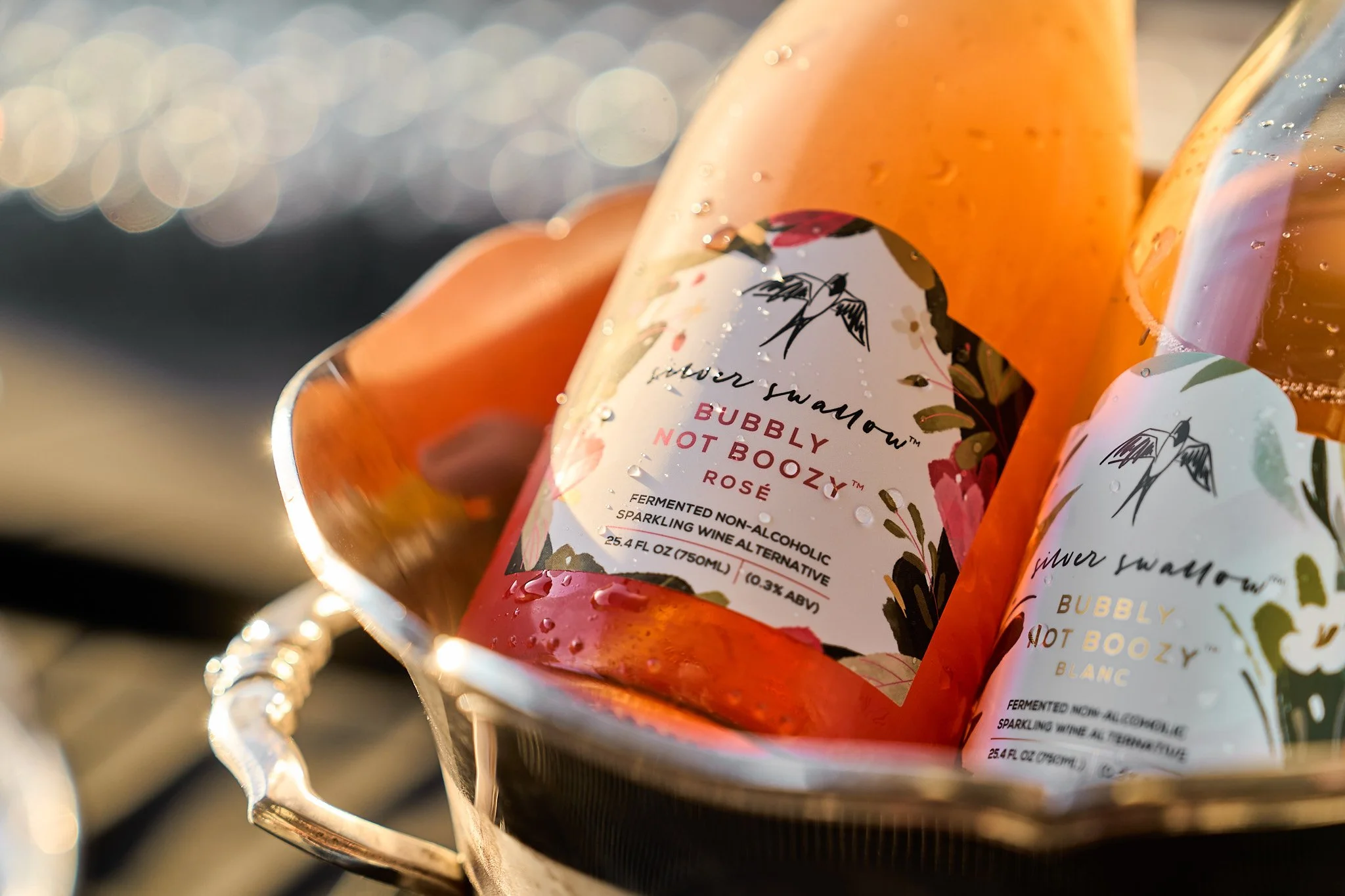 Close-up of cans of sparkling non-alcoholic wine, Silver Swallow, in a silver bucket with water droplets, with a blurred background. Photographed by Gumption Studio, Ottawa event photographer.