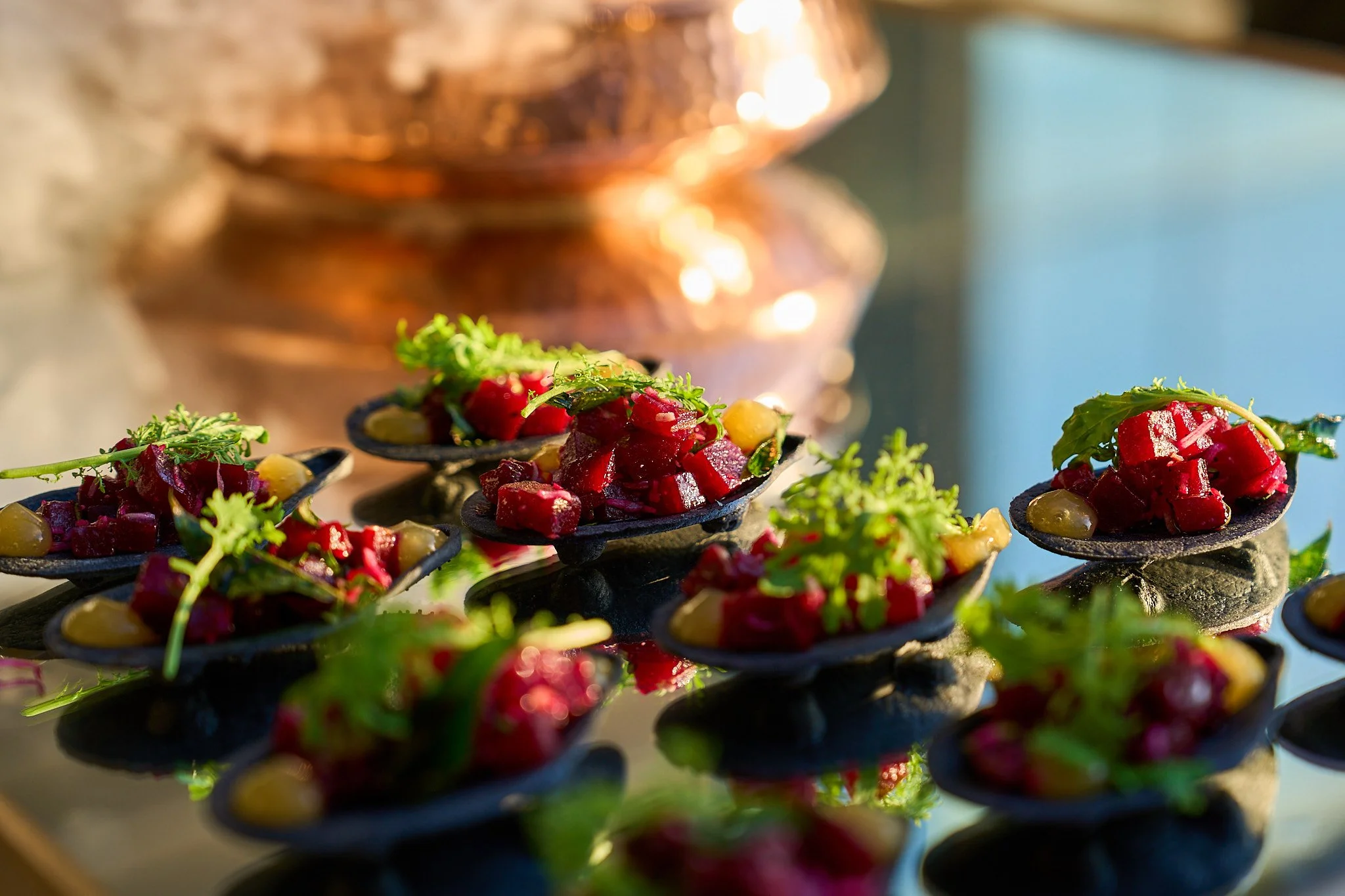 Close-up of a beet dish from Harvest: Feast of Fall garnished with fresh herbs on small black dishes, with a blurred background of warm lighting. Photographed by Gumption Studio, Ottawa event photographer.