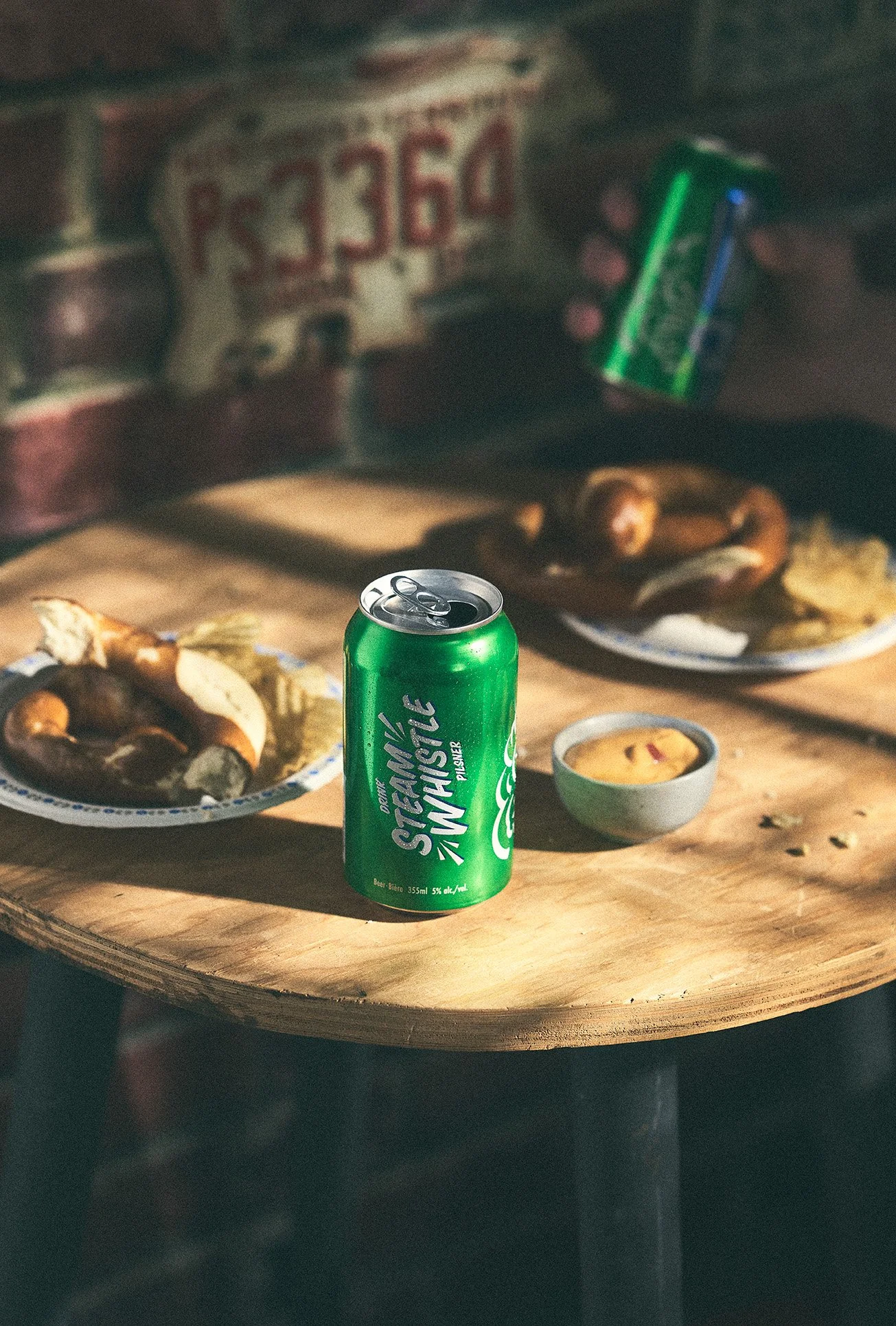 A green can of Steam Whistle on a wooden surface, with plates of pretzels. Photographed by Nick Ghattas, set stylist is Gumption Studio.