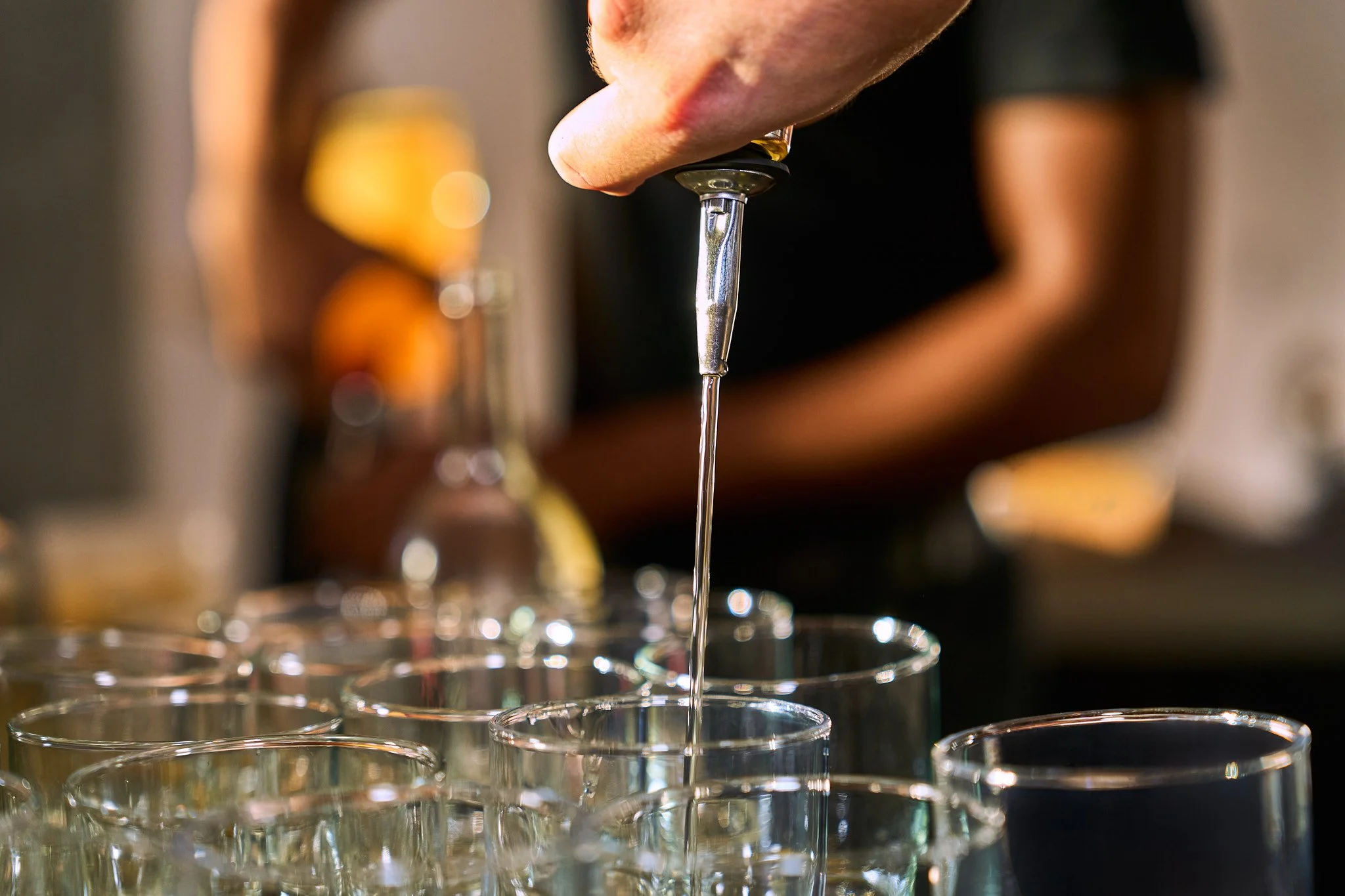 A close-up of a person filling a shot glass with clear liquid from a pour spout, with additional shot glasses in the background. Photographed by Gumption Studio, Ottawa event photographer.