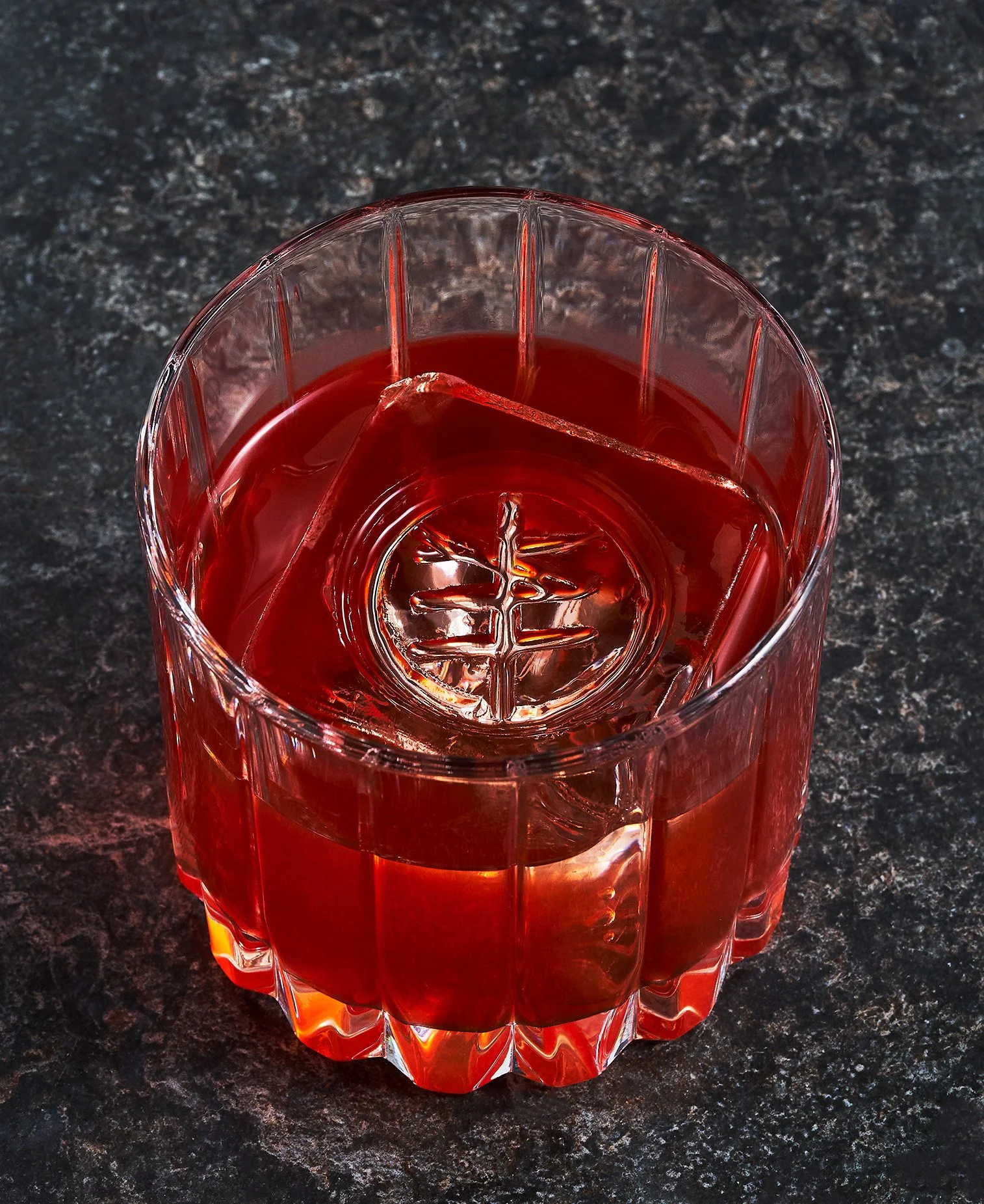 Lost in Migration cocktail with ice cubes on a dark, speckled countertop. Photographed for the Perch Cookbook by Gumption Studio, Ottawa Cookbook photographer.