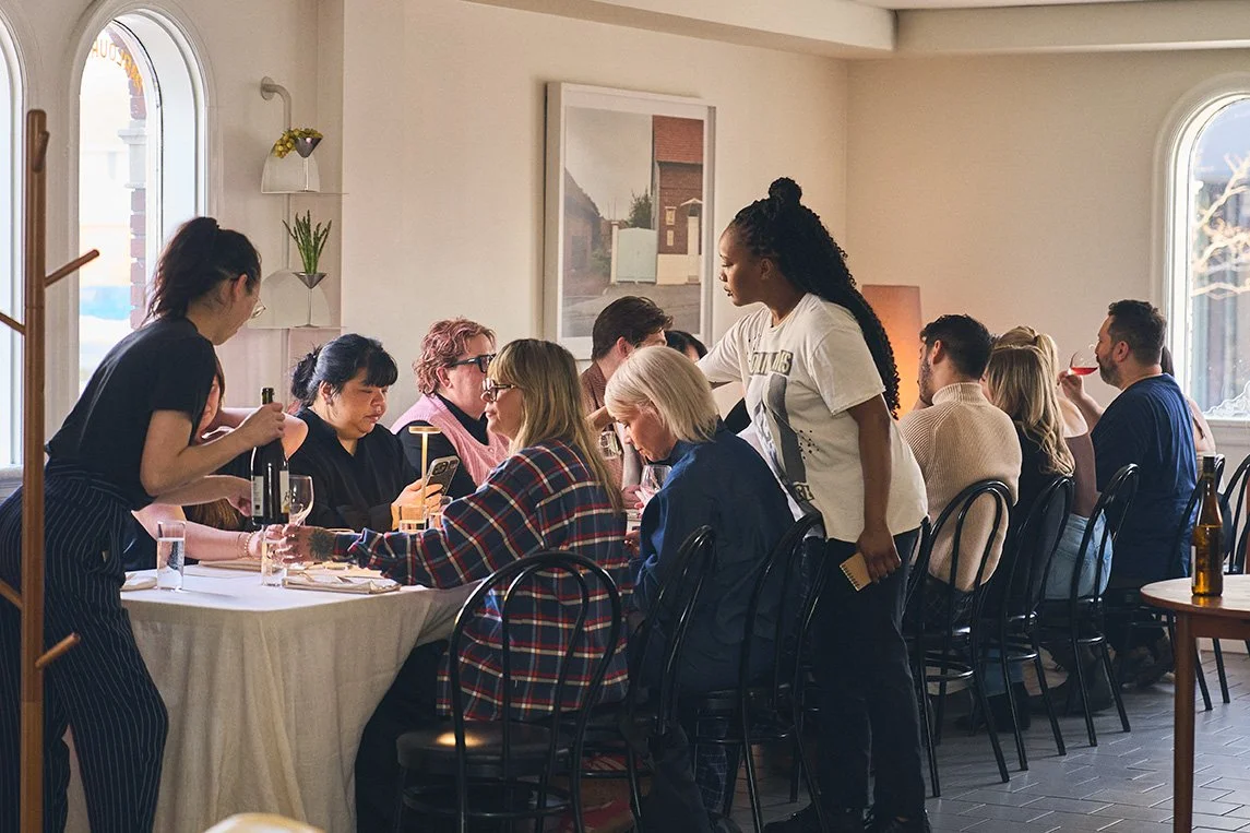 A diverse group of people dining at a restaurant during the daytime, with waitstaff serving them.