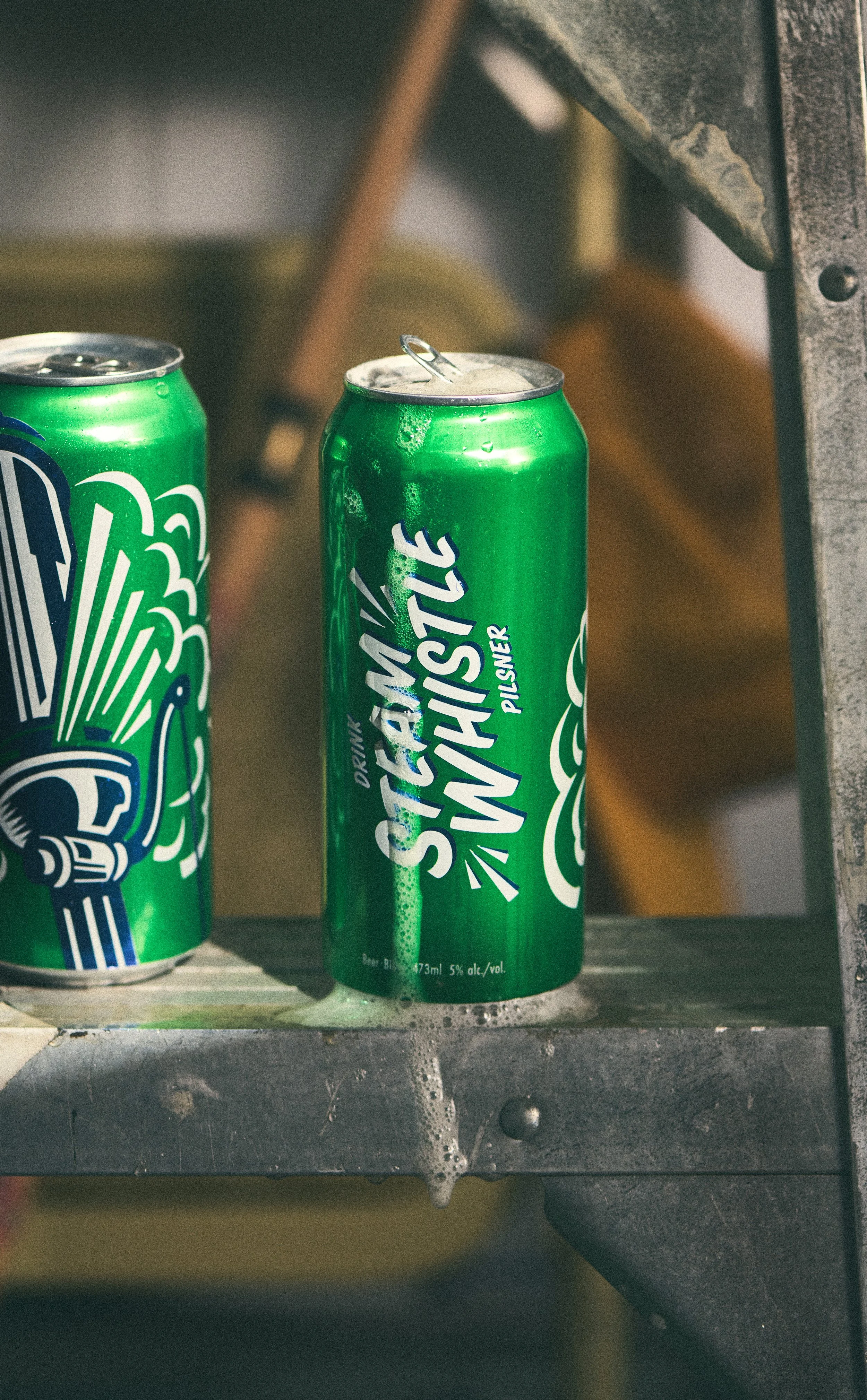 A can of Steam Whistle on a metal surface with condensation and a partially open tab. Photographed by Nick Ghattas, set stylist is Gumption Studio.