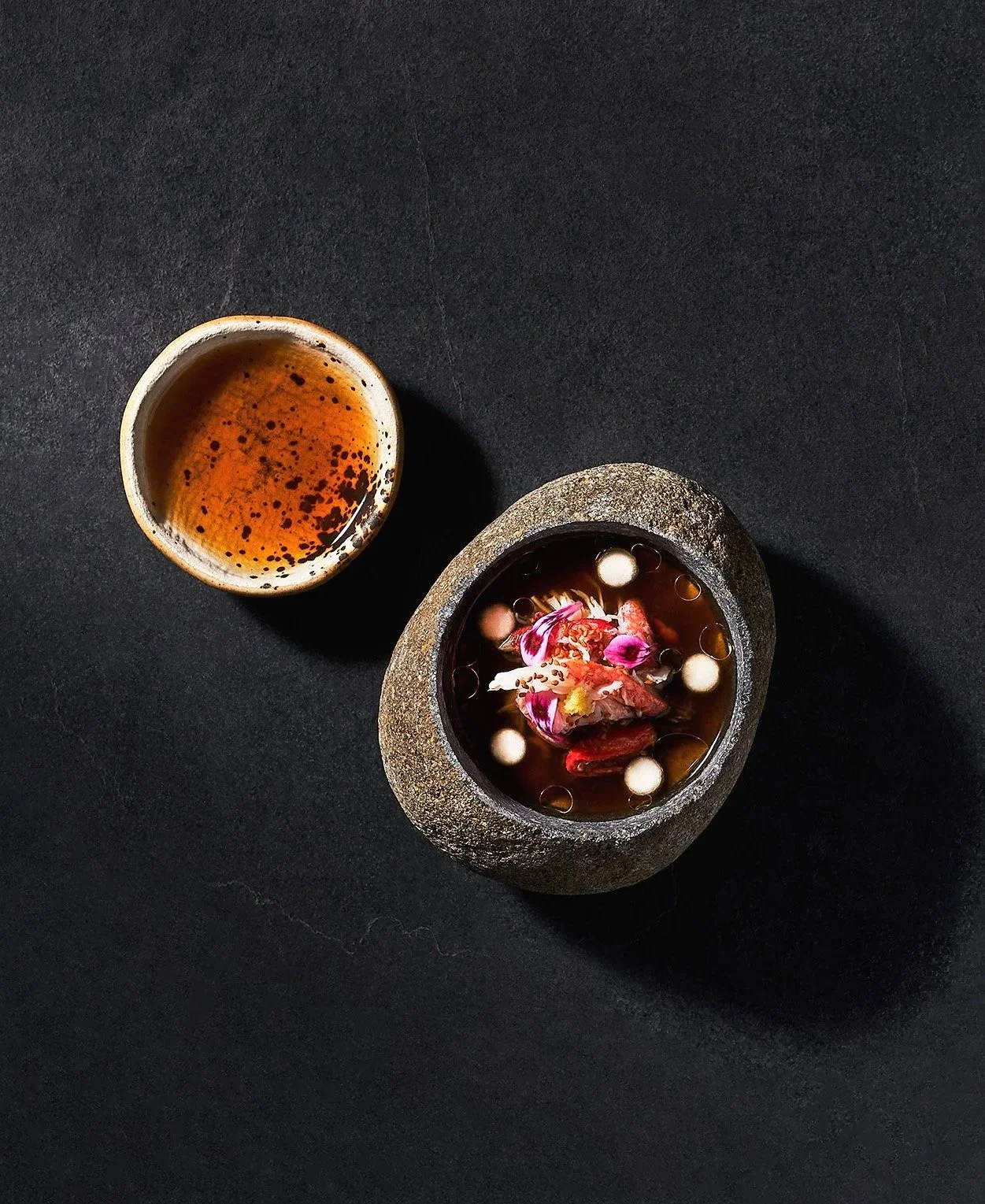 A chawanmushi by Justin Champagne-Lagarde in a stone bowl garnished with edible flowers on top. Photographed for the Perch Cookbook by Gumption Studio, Ottawa Cookbook photographer.