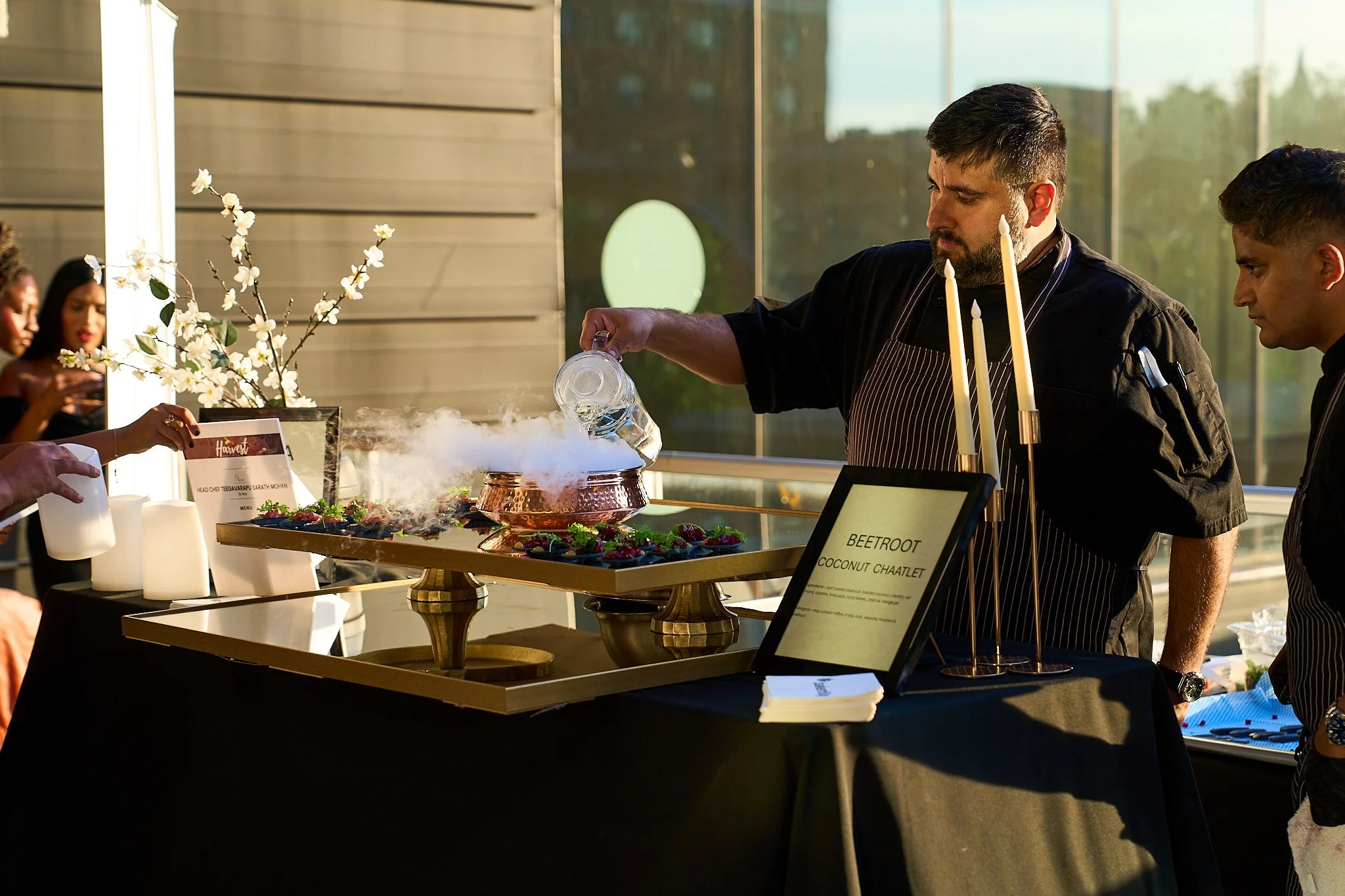 A chef pouring water on a dry ice on a dish at Harvest: A Feast of Fall with some guests in the background. Photographed by Gumption Studio, Ottawa event photographer.