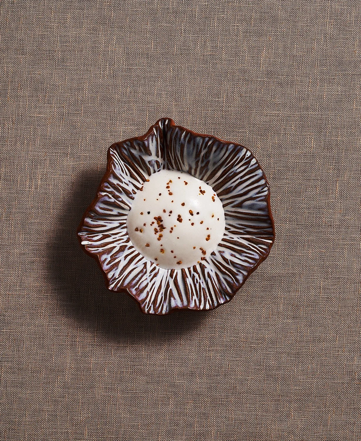 A decorative ceramic bowl with a ruffled edge, with a Goose Heart Raviolo. Photographed for the Perch Cookbook by Gumption Studio, Ottawa Cookbook photographer.