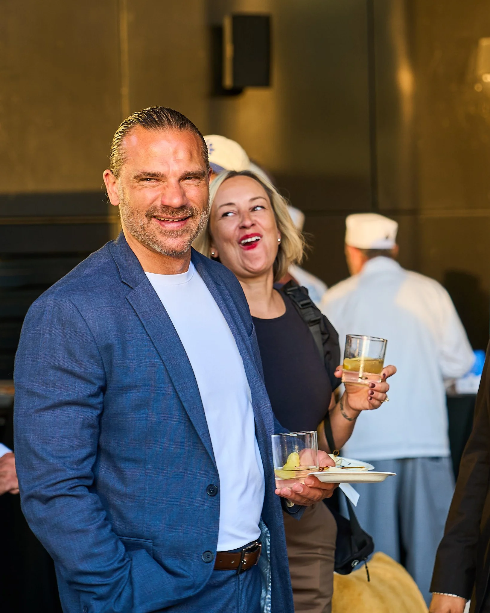 A man in a blue blazer and white shirt holding a glass with a yellow beverage at Harvest: A Feast of Fall. Photographed by Gumption Studio, Ottawa event photographer.
