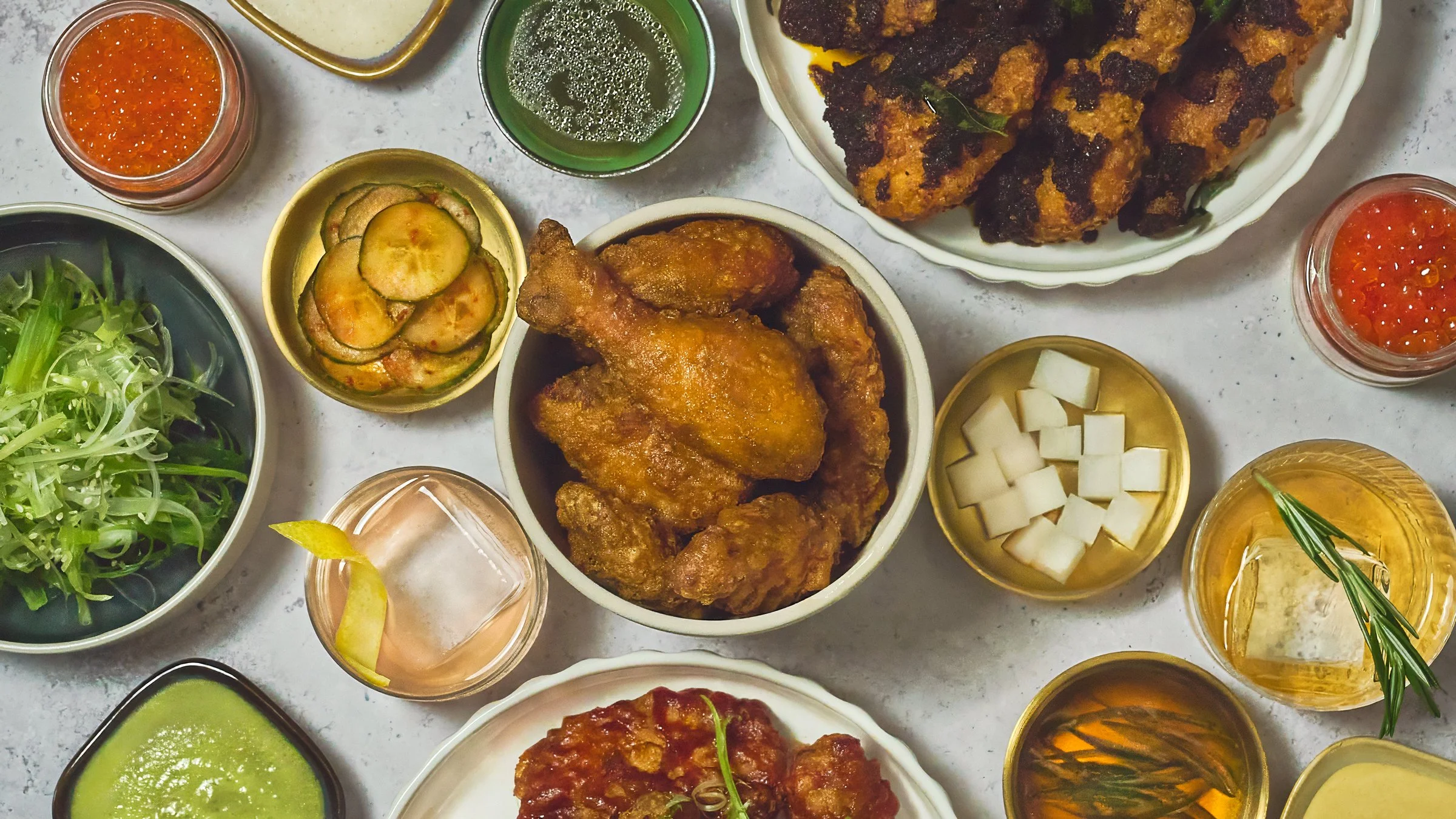 Assorted dishes of fried chicken, salad, pickles, and condiments on a white table at Kozhi Restaurant. Brand Identity by Gumption studio.