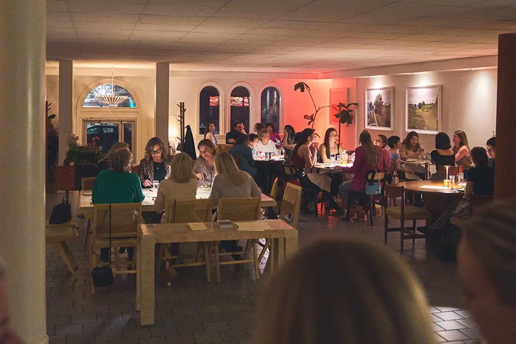 People dining at tables at Parlour for Girl Dinner with large arched windows and landscape paintings on the wall. Photographed by Gumption Studio, Ottawa event photographer.