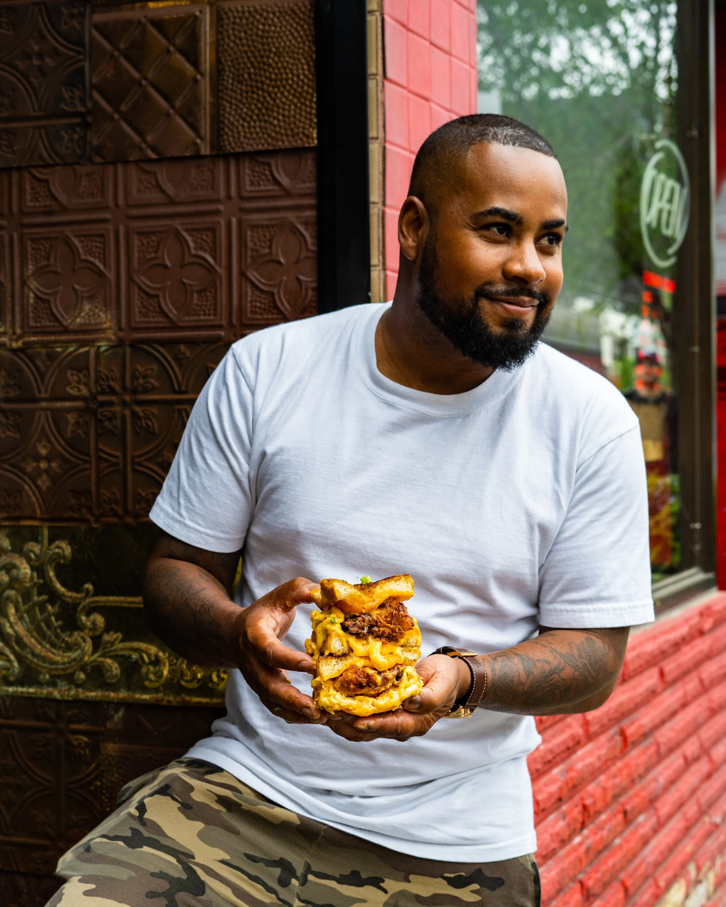 Jerome Robinson holding a large fried chicken grilled cheese with purple slaw by the Heartbreak Chef. Photographed by Gumption Studio, Toronto food photographer.